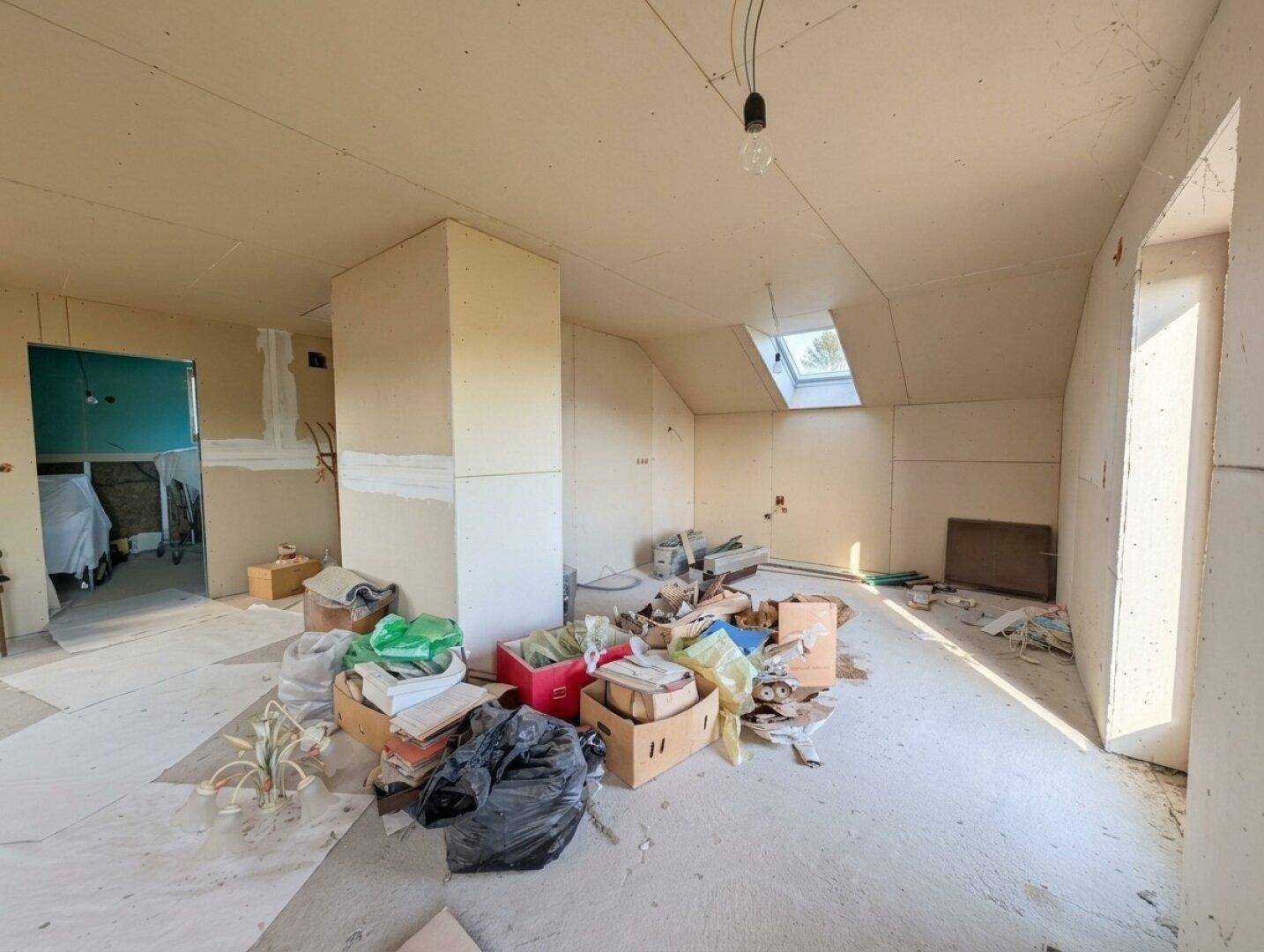 Unfertiger Dachgeschossraum mit Baumaterialien und Schutt, bereit für den weiteren Ausbau.