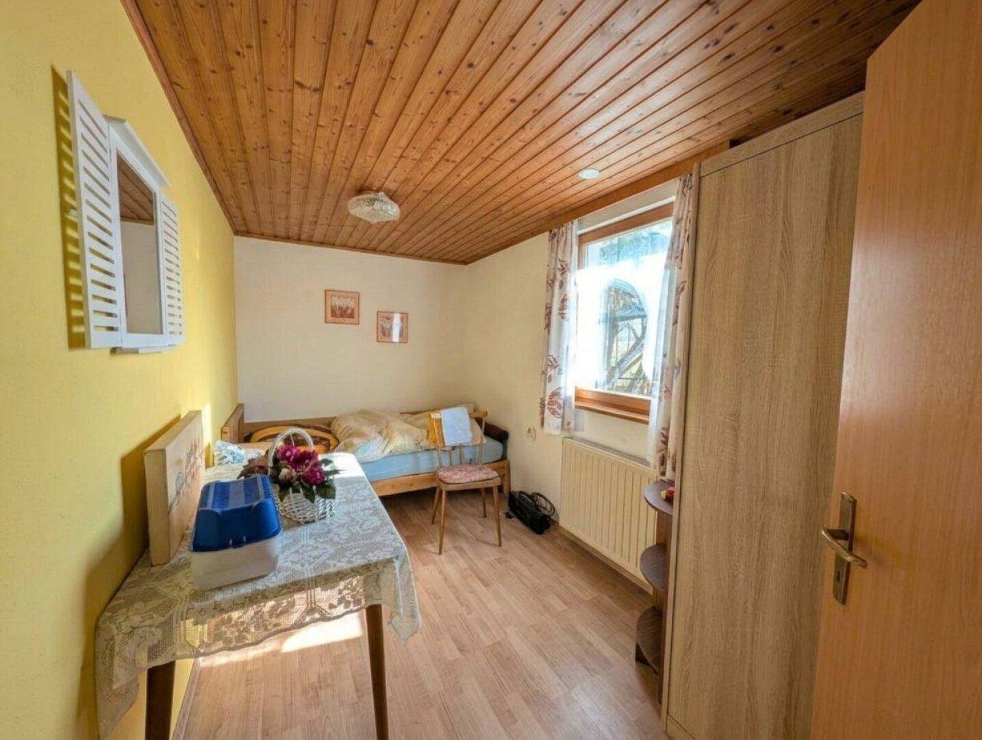 Kleines Schlafzimmer mit Holzbalkendecke, Parkettboden und einem Fenster.