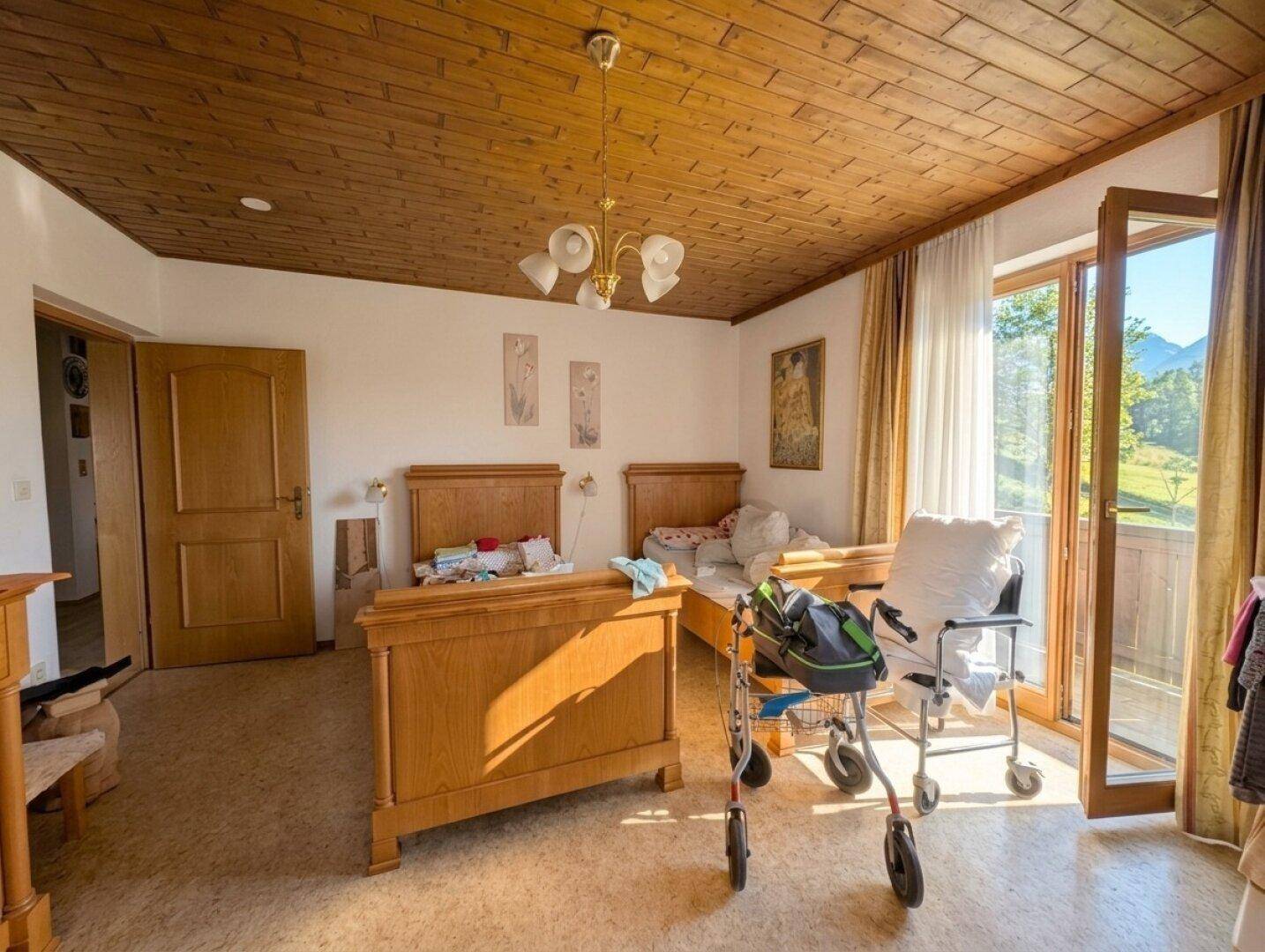 Helles Schlafzimmer mit Holzdecke, zwei Einzelbetten und Zugang zu einem Balkon mit Bergblick.