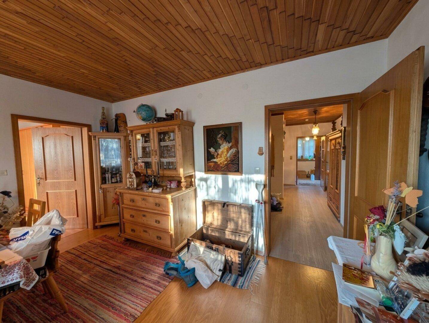 Gemütlicher Wohnbereich mit Holzdecke, traditionellen Holzmöbeln und Teppichboden in warmen Farben.