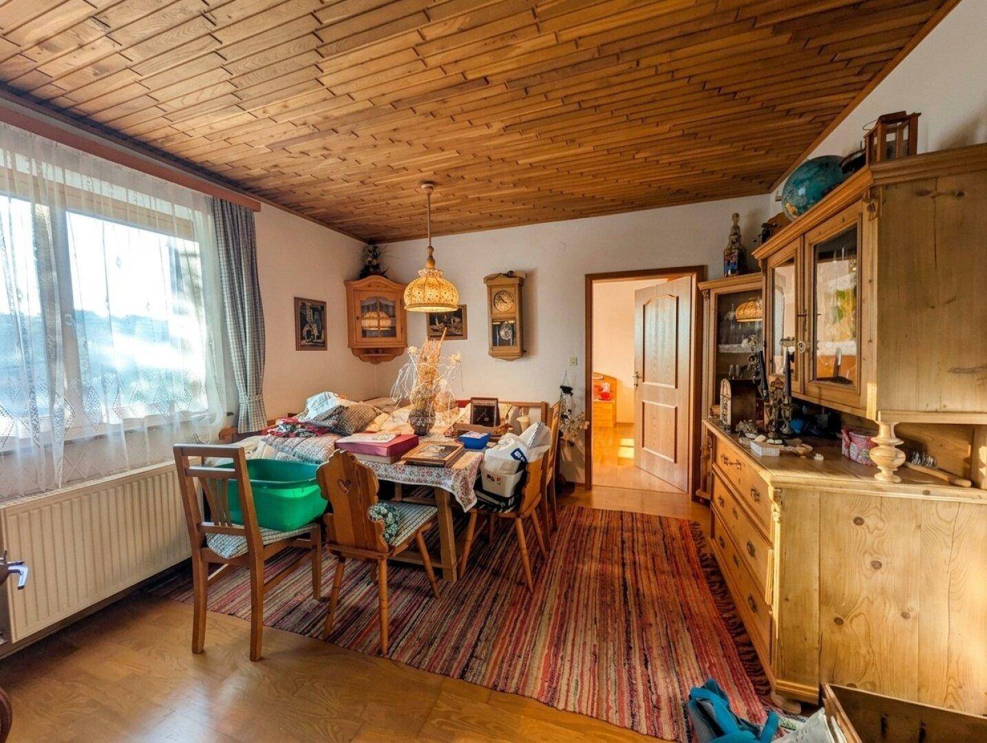 Essbereich mit Holzdecke, großem Esstisch und traditionellen Holzstühlen, beleuchtet durch ein Fenster.