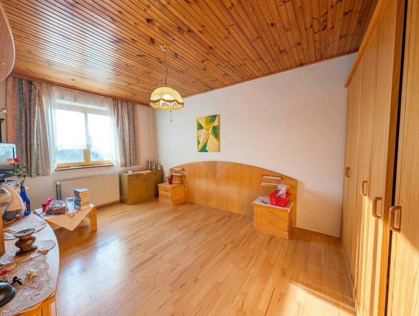 Helles Schlafzimmer mit Holzbalkendecke, Parkettboden und großem Fenster.