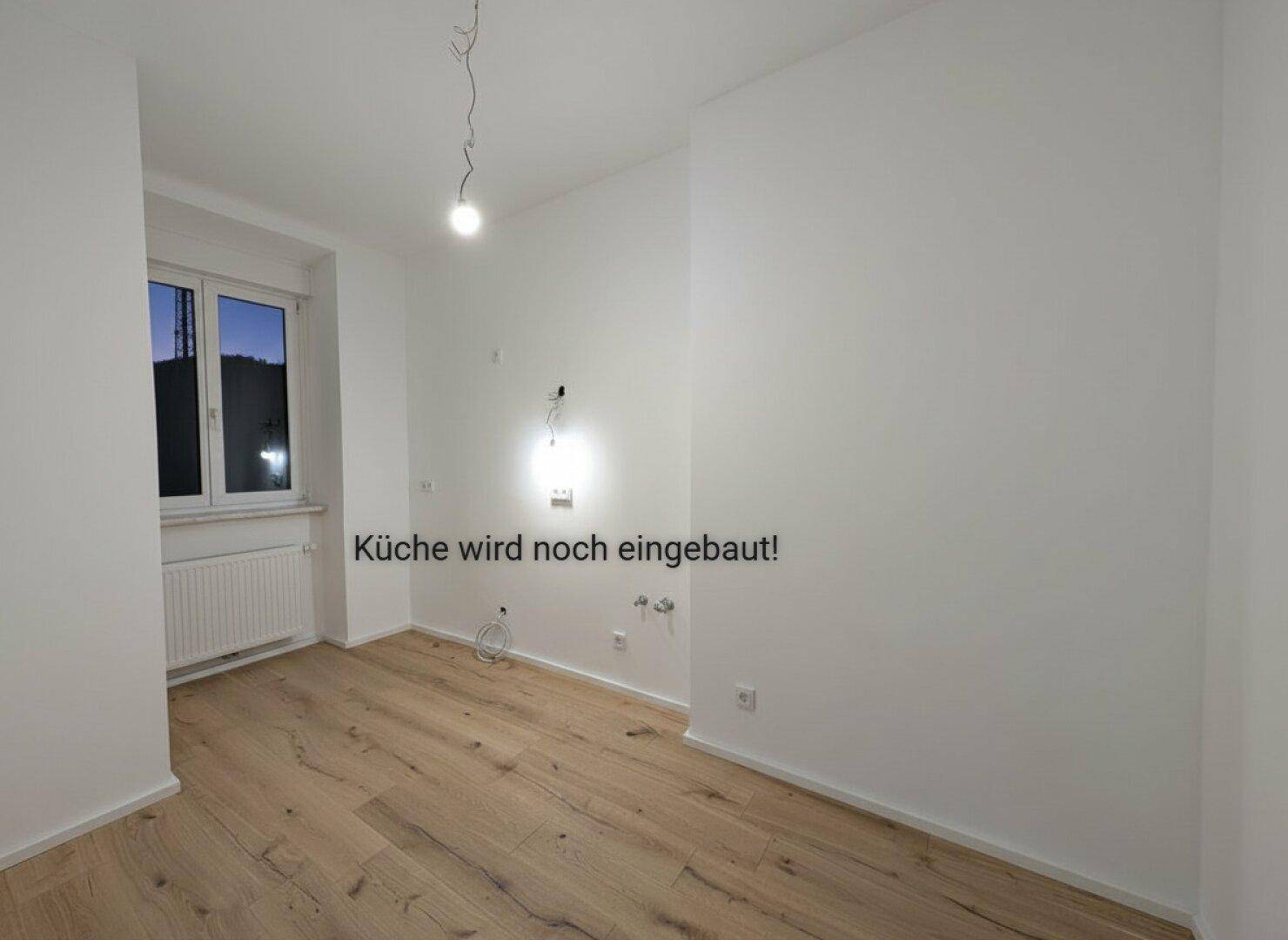 Leerer Küchenraum mit Holzboden und Fenster, vorbereitet für den Einbau einer neuen Küche.