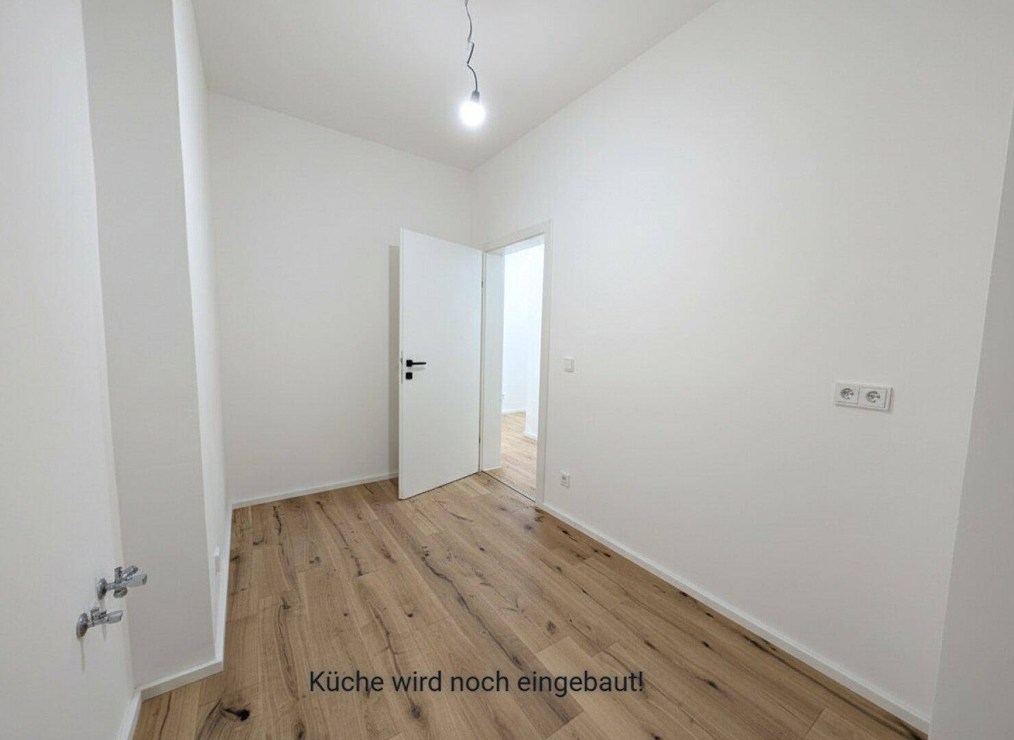 Geräumiger Küchenbereich mit Holzboden und weißen Wänden, bereit für die Installation der Küche.