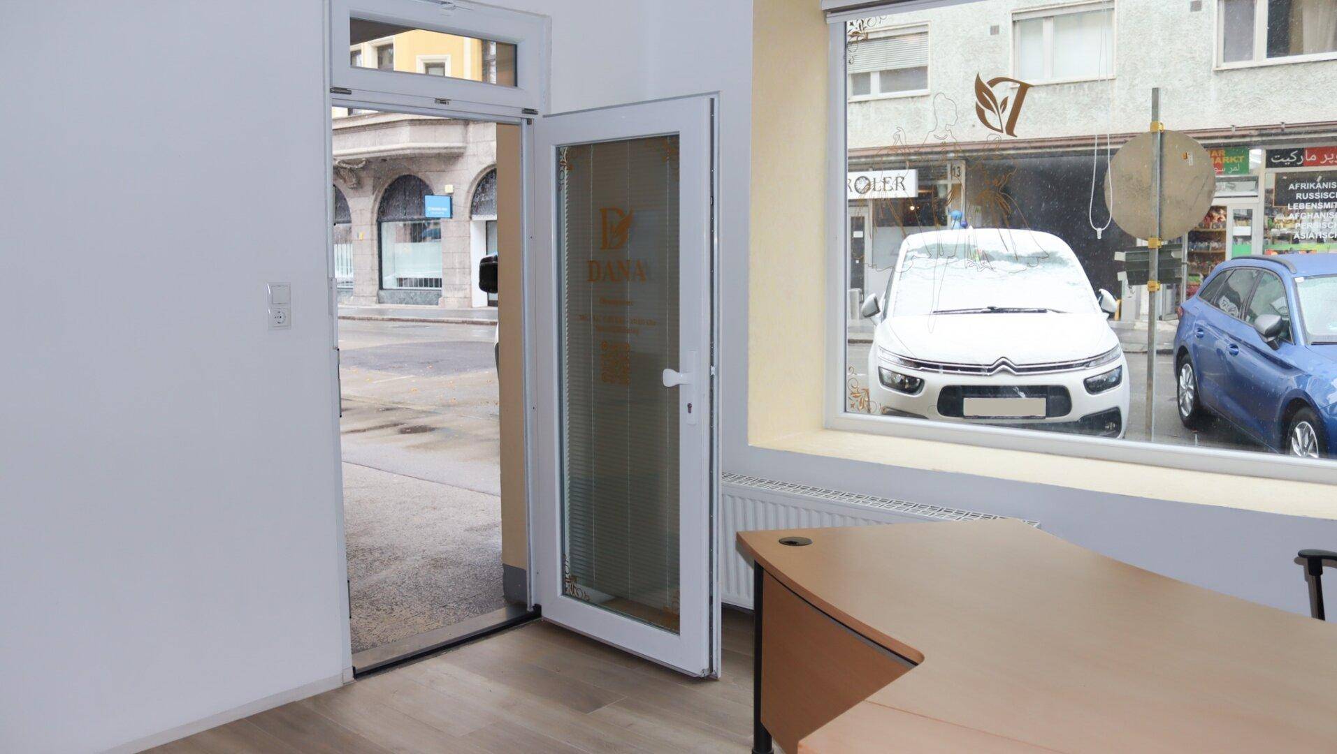 Büroraum mit einer Glastür zum Eingangsbereich und einem Fenster mit Blick auf die Straße.