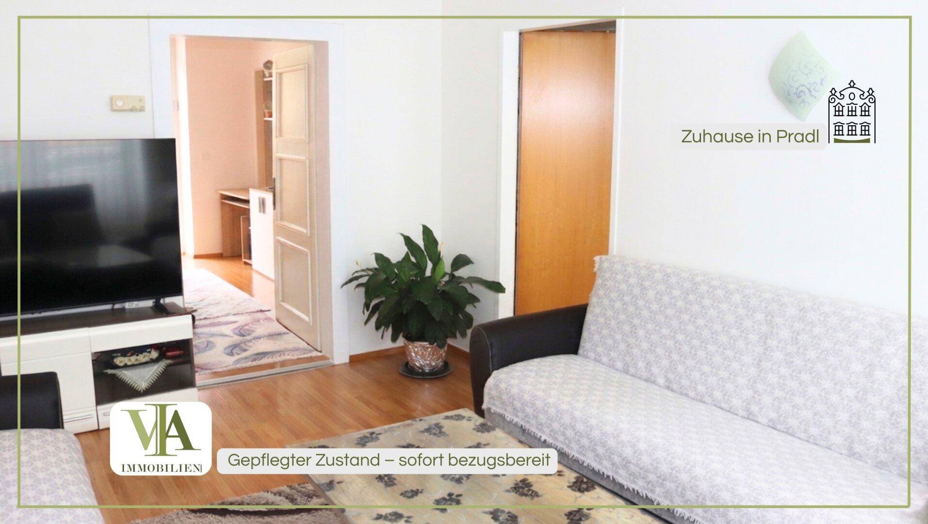 Gemütliches Wohnzimmer mit Sofa, Fernseher und Zugang zu weiteren Räumen.