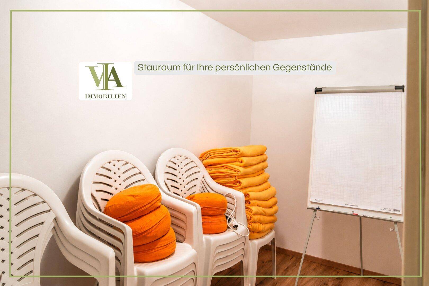 Kleiner Raum mit weißen Plastikstühlen, orangefarbenen Kissen und einem Flipchart, als Abstellraum nutzbar.