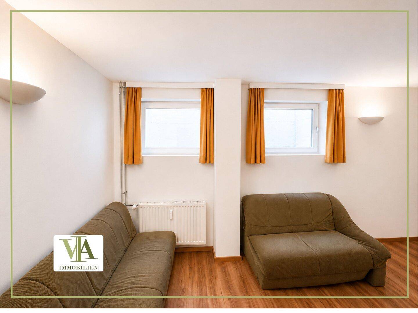 Gemütlicher Wohnbereich mit zwei Sofas, Laminatboden und Fenstern mit gelben Vorhängen.
