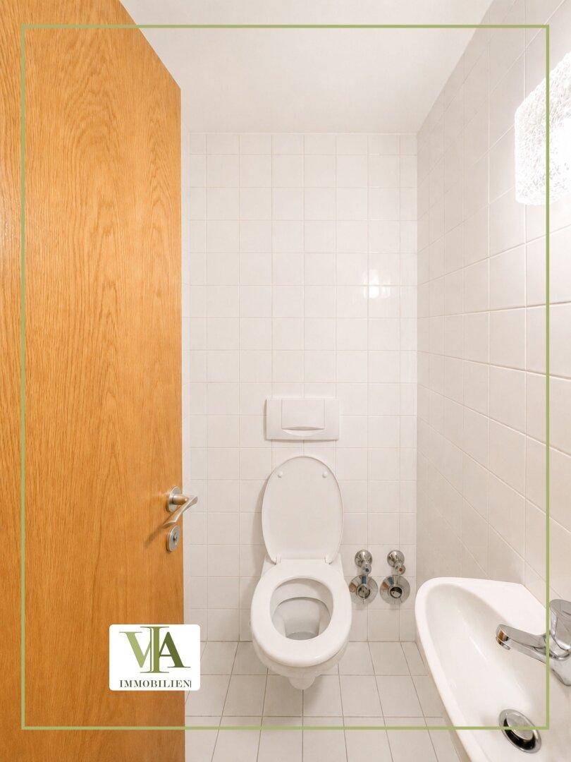 Gefliestes WC mit wandmontierter Toilette und kleinem Waschbecken, in gutem Zustand.