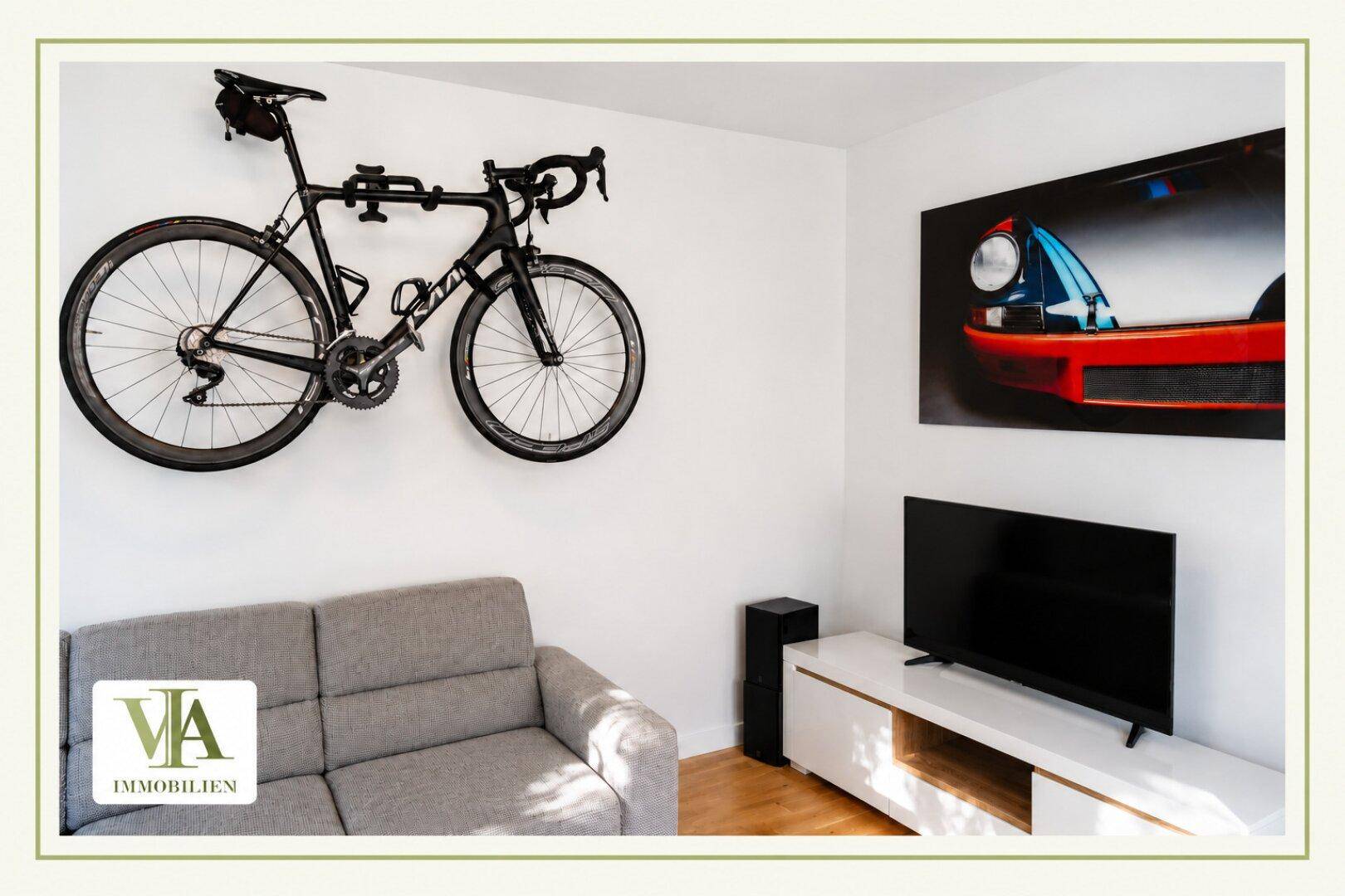 Wohnzimmer mit Sofa, Fernseher und einem an der Wand montierten Fahrrad.