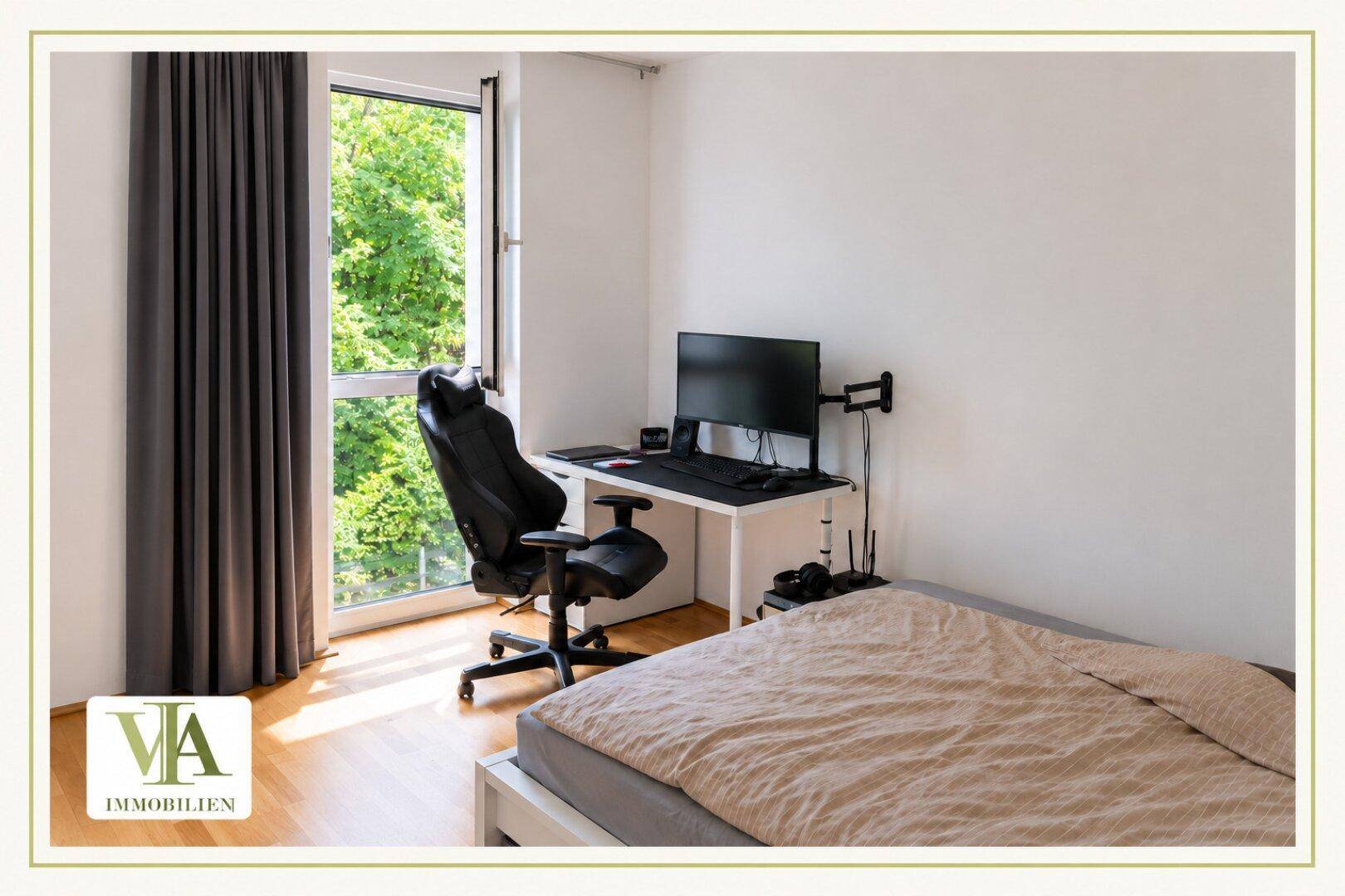 Schlafzimmer mit Holzboden, Schreibtisch und großem Fenster mit Blick ins Grüne.