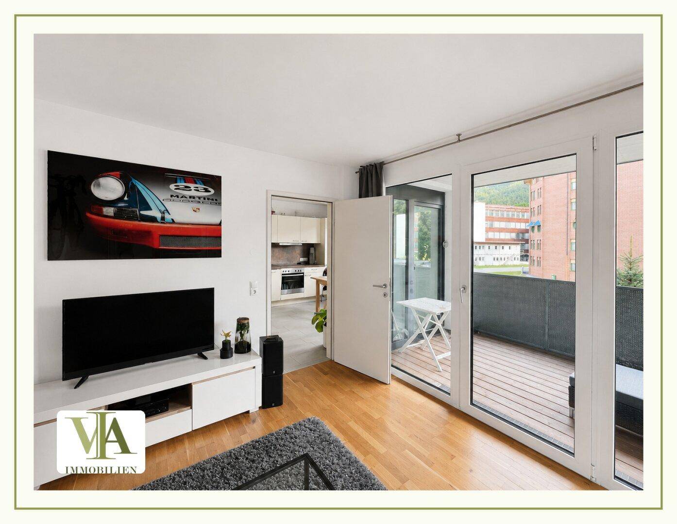 Helles Wohnzimmer mit Holzboden, Fernseher und großem Zugang zum Balkon.