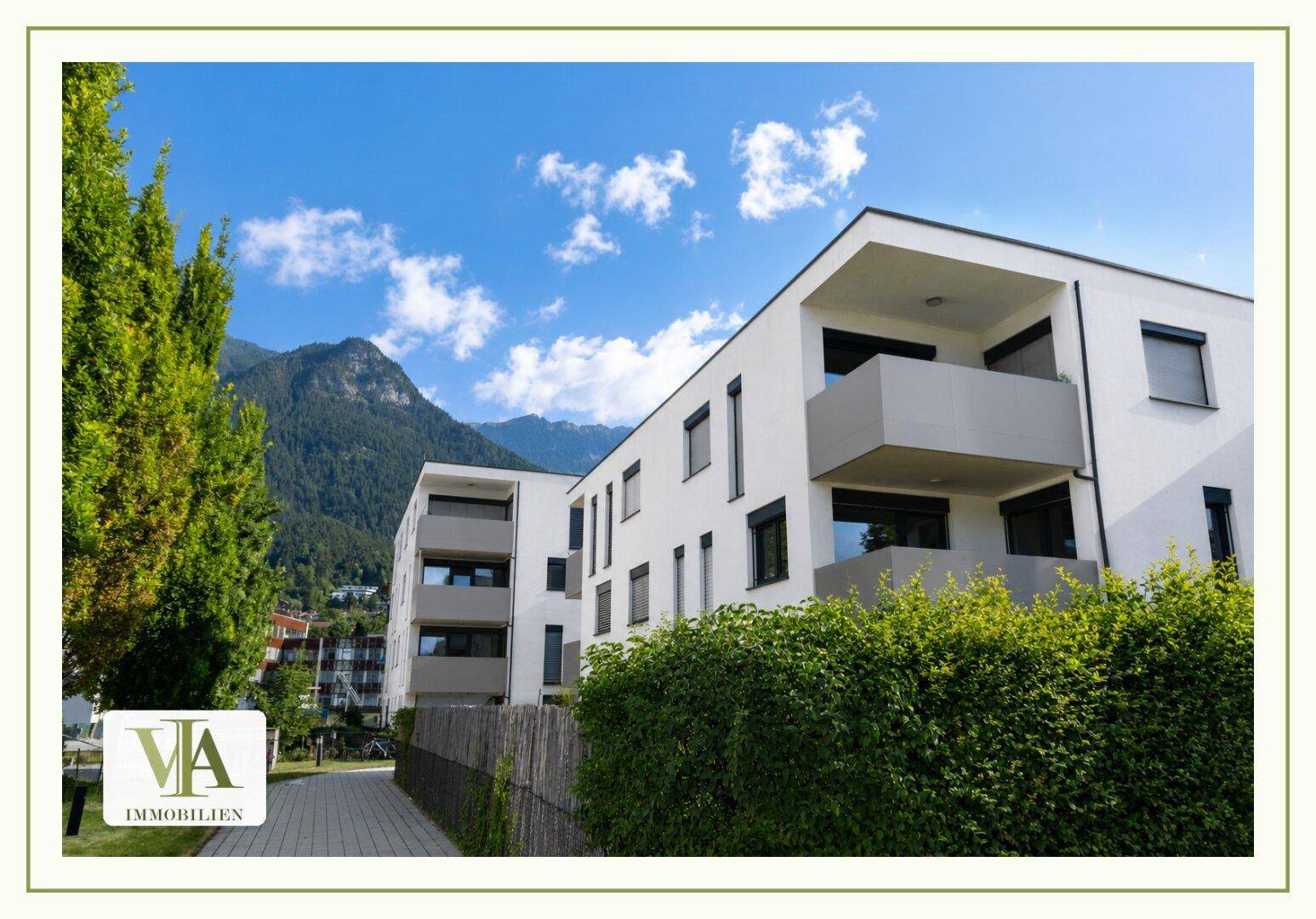 Modernes Wohngebäude mit grüner Umgebung und beeindruckendem Bergblick im Hintergrund.