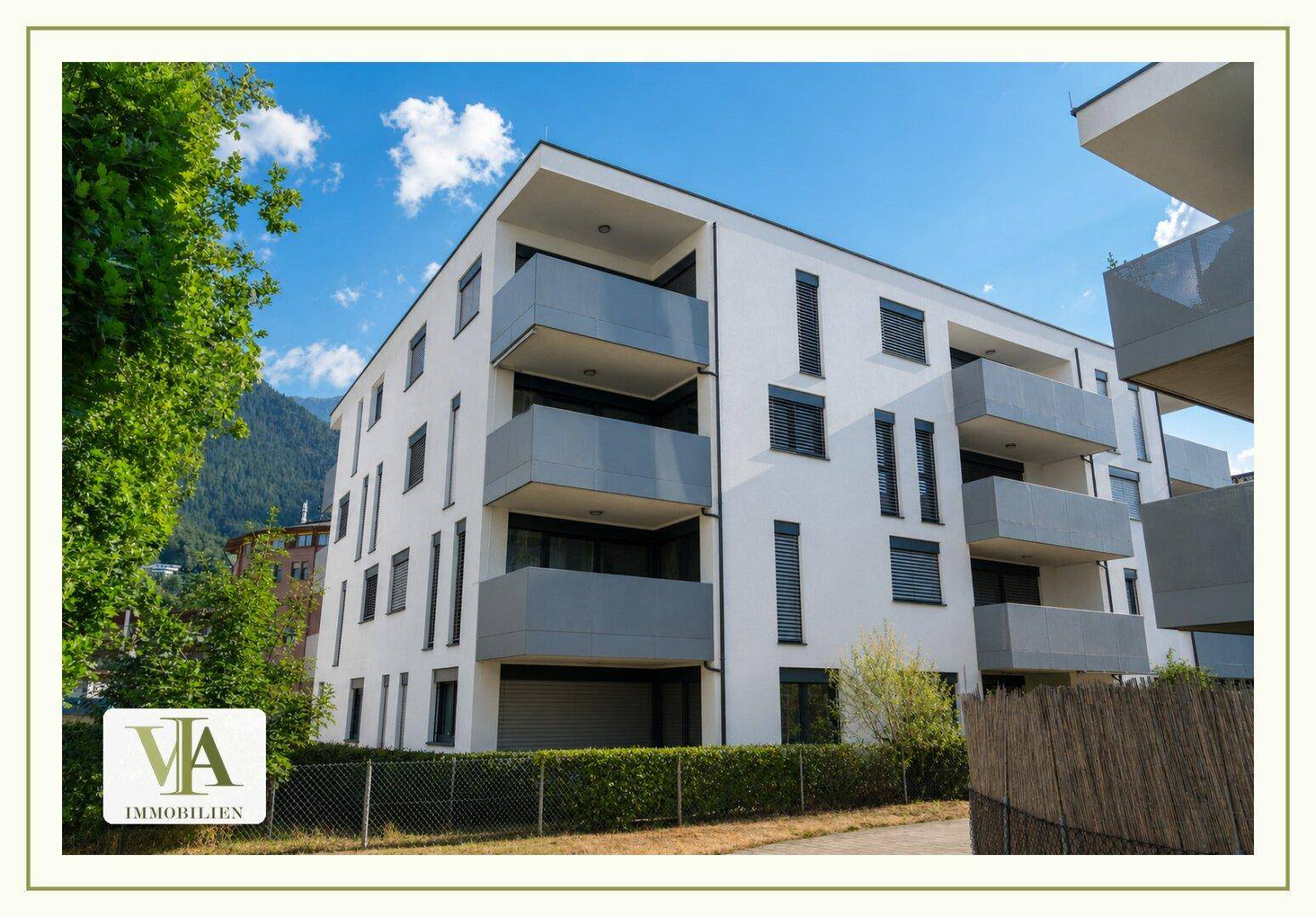 Modernes Mehrfamilienhaus mit weißer Fassade und grauen Balkonen unter blauem Himmel.