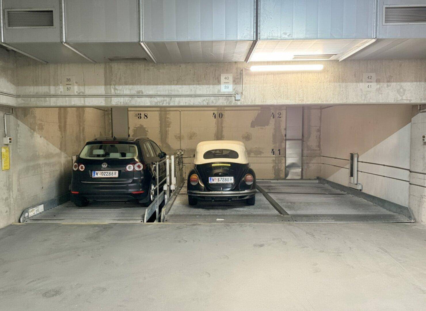 Zwei Autos parken auf Doppelparkern in einer gut beleuchteten Tiefgarage.