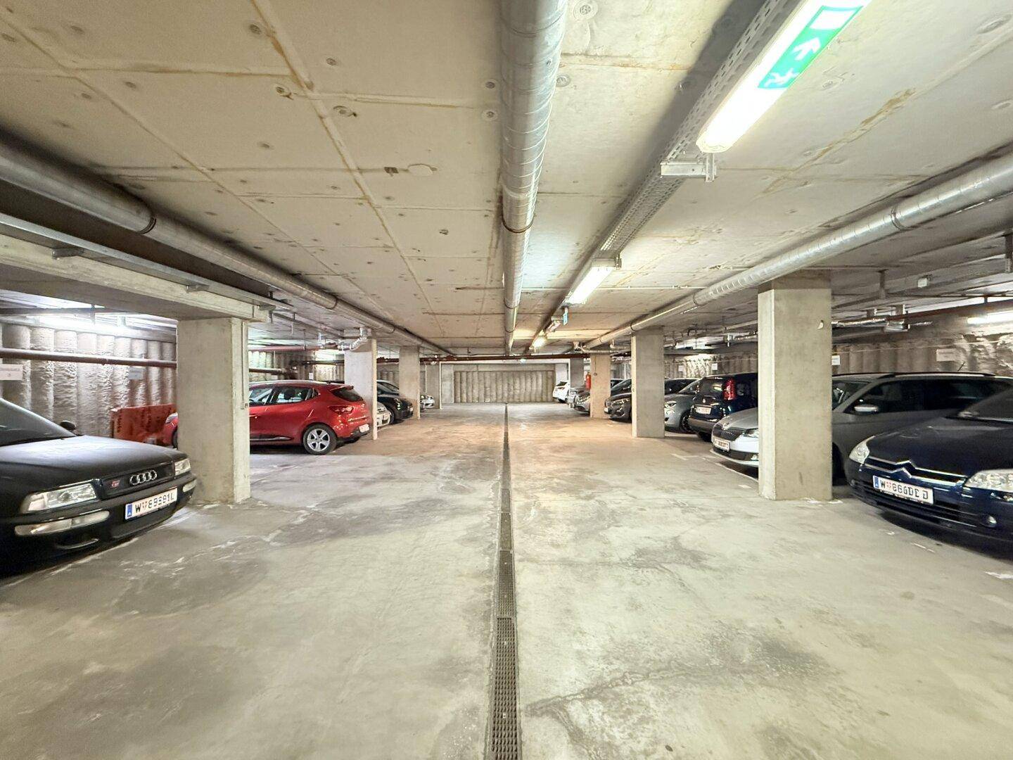 Weitläufige Tiefgarage mit vielen Parkplätzen, Betonpfeilern und sichtbaren Installationen an der Decke.