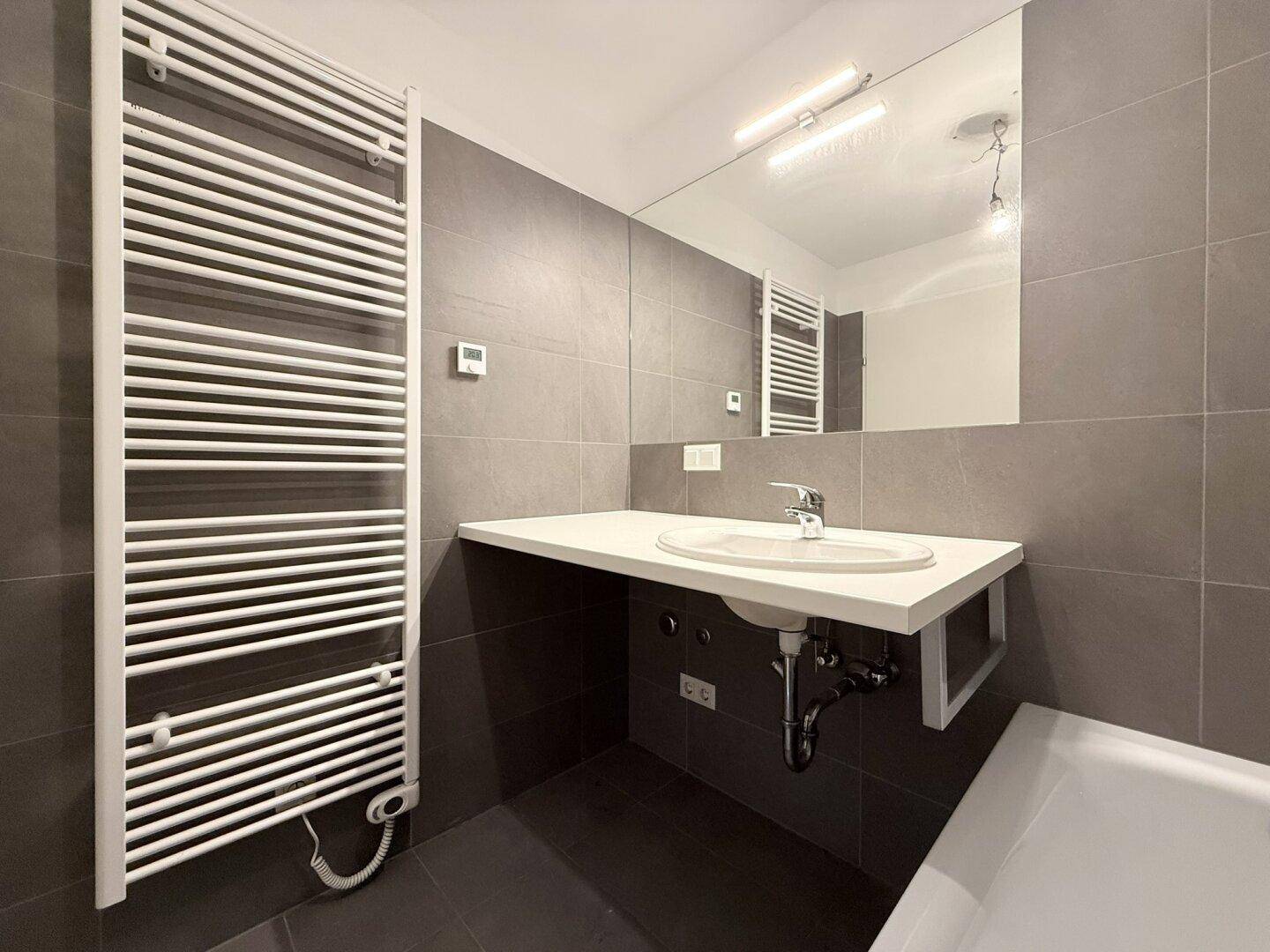 Modernes Badezimmer mit Badewanne, Waschbecken und beheiztem Handtuchhalter.