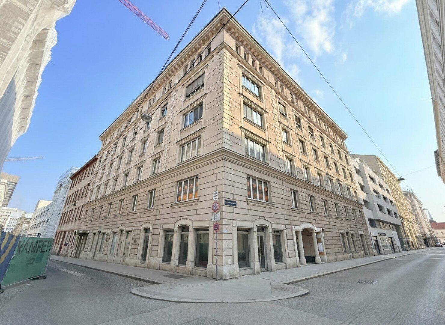 Weitwinkelansicht eines mehrstöckigen Eckgebäudes mit traditioneller Architektur und umliegender Stadtlandschaft.