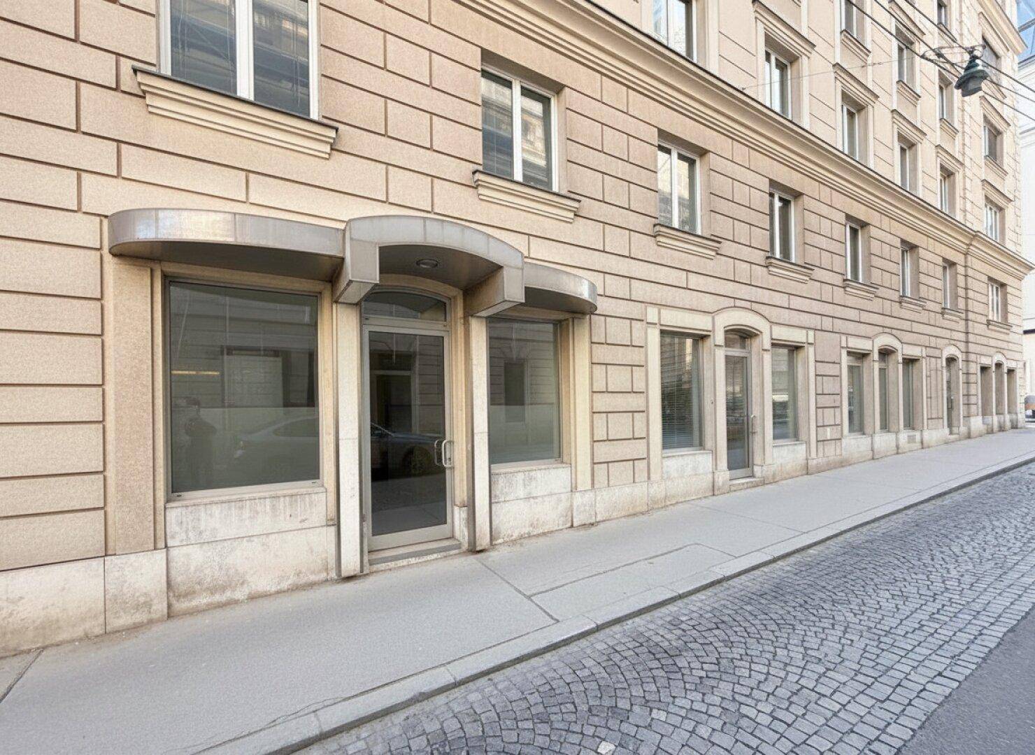 Erdgeschossfassade mit großen Schaufenstern und einem Eingang an einer Kopfsteinpflasterstraße.