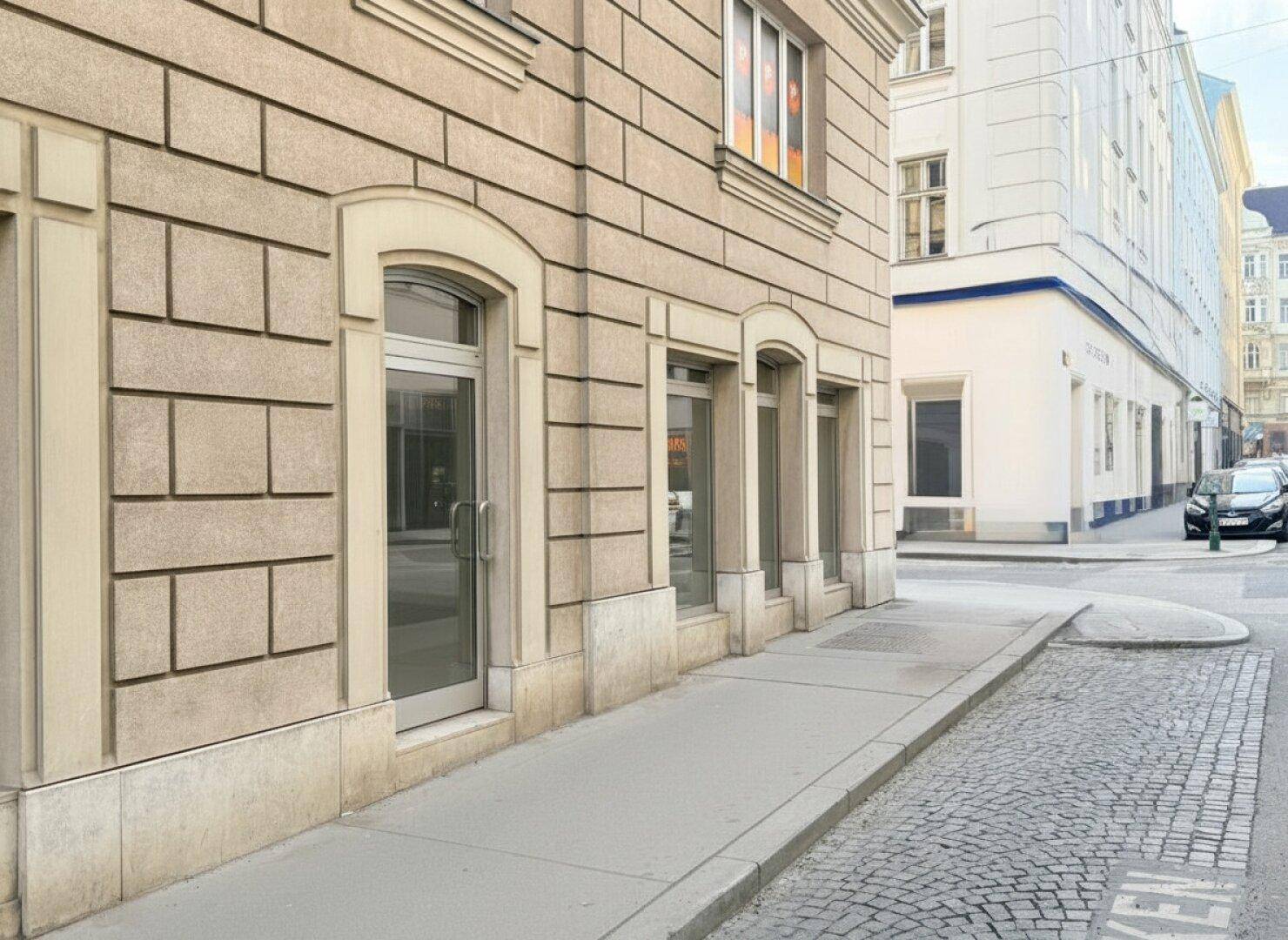Gebäudeecke mit großen Bogenfenstern und einem Eingang an einer ruhigen Seitenstraße.