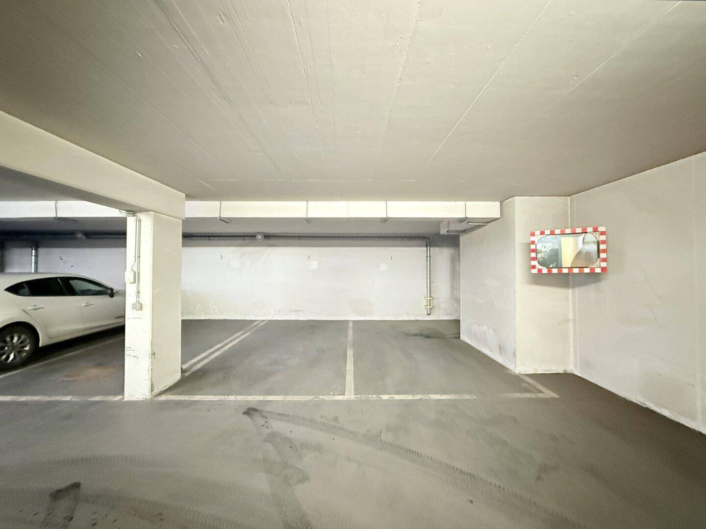 Leerer Tiefgaragenstellplatz mit einem Konvexspiegel zur besseren Übersicht und hellen Wänden.