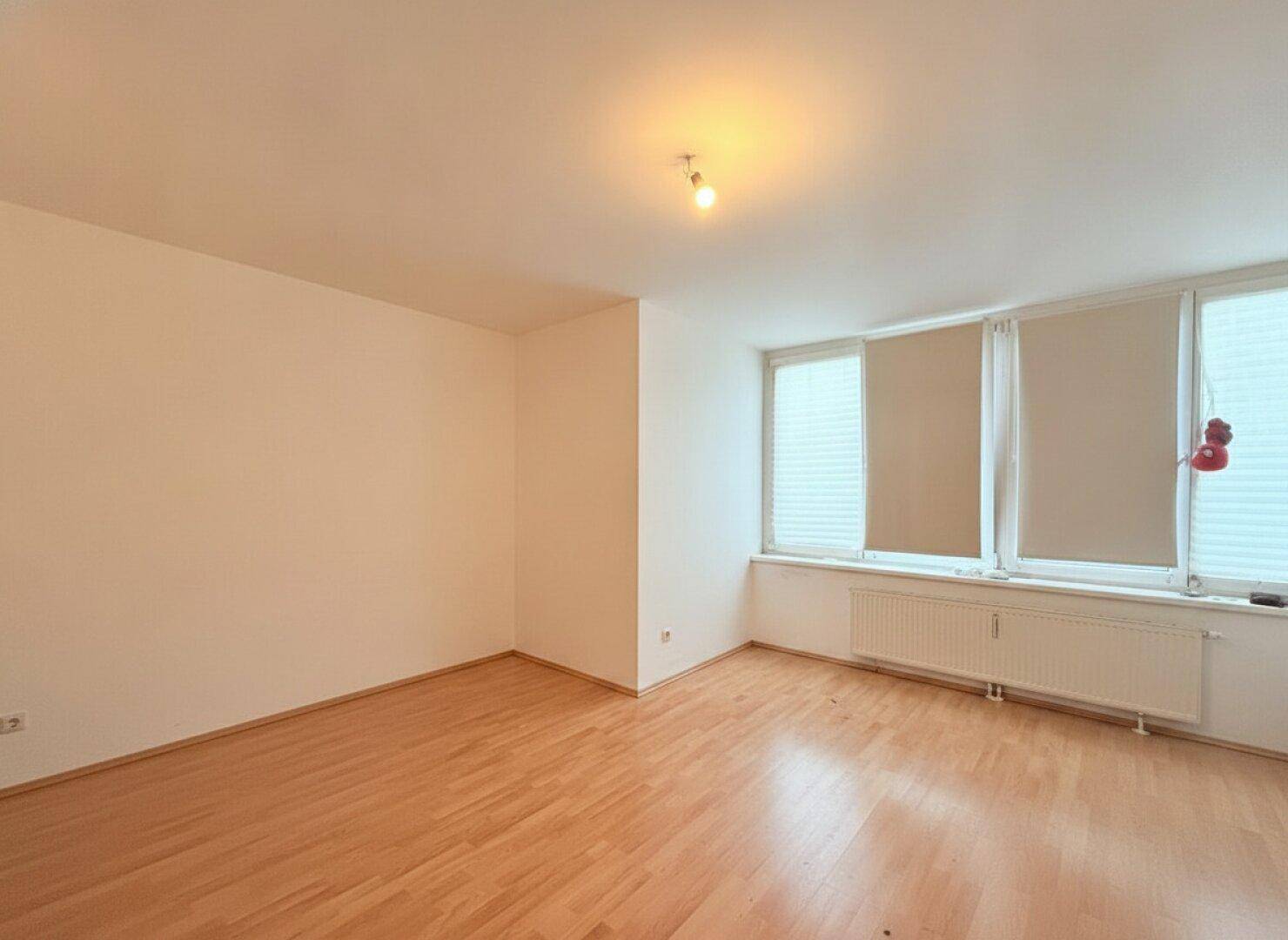 Geräumiges, helles Zimmer mit Parkettboden und Fensterfront, ideal als Wohn- oder Schlafzimmer.