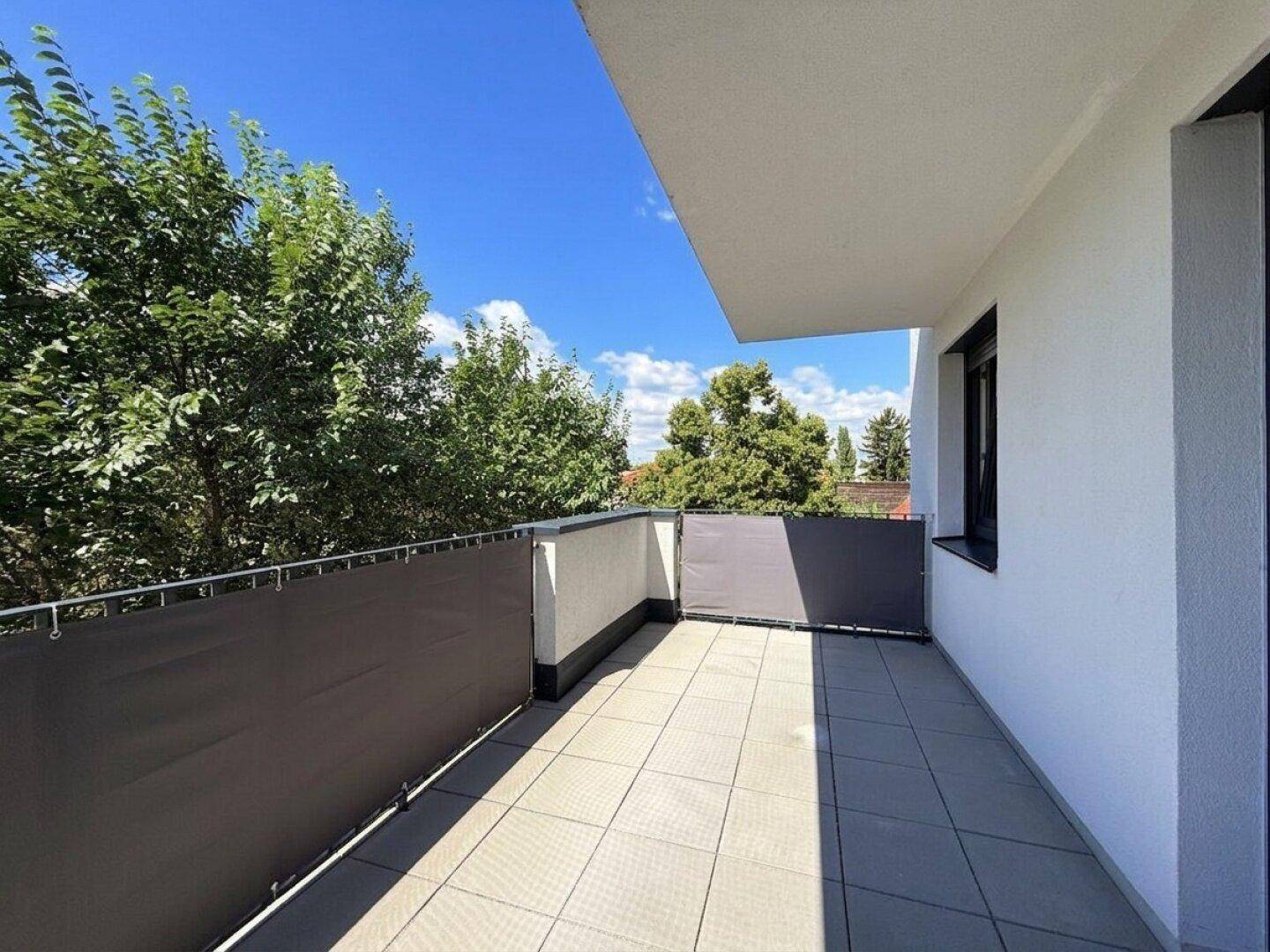 Sonniger Balkon mit Fliesenboden und Blick auf Bäume, ideal für entspannte Stunden im Freien.