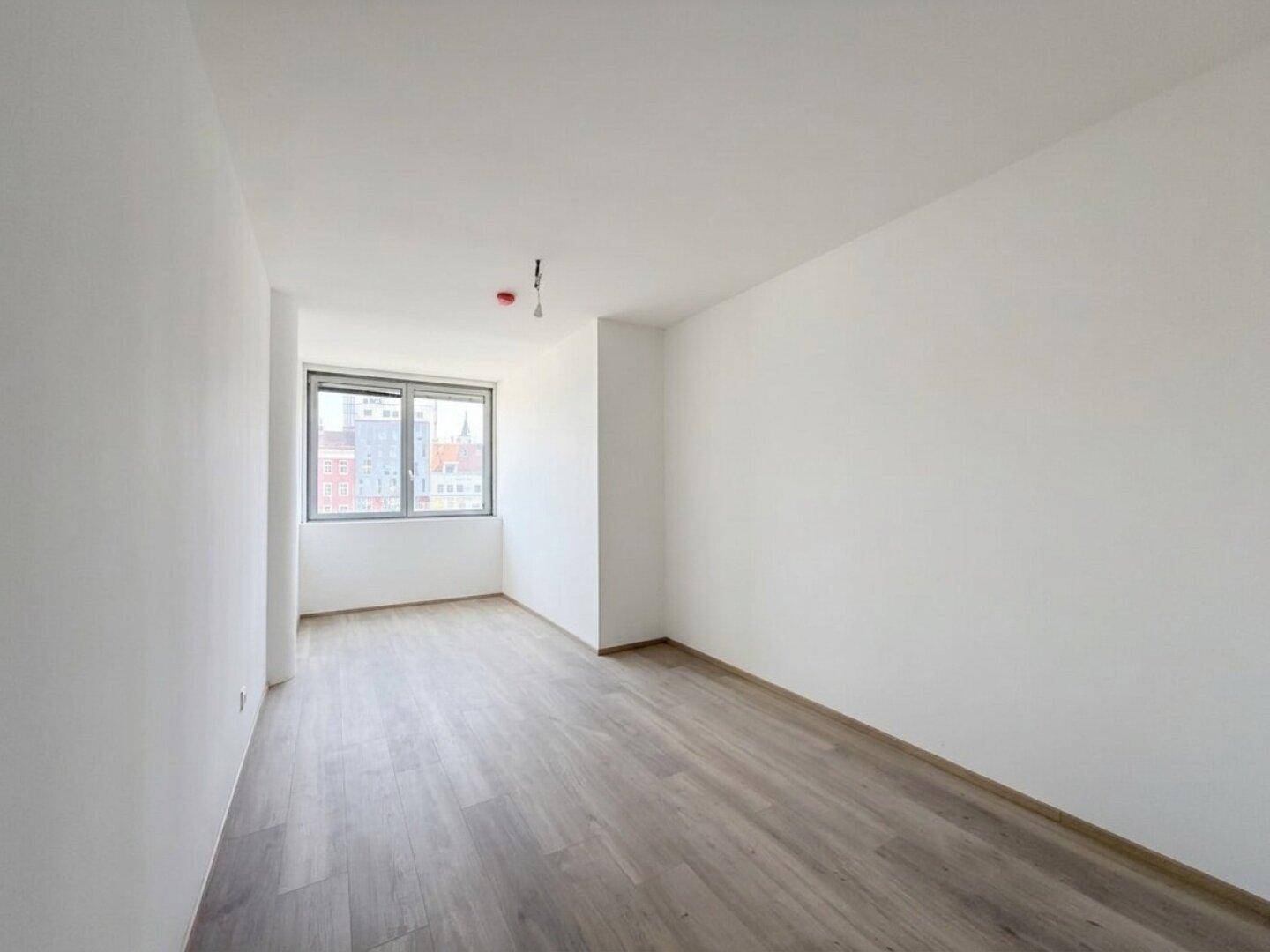 Geräumiger, heller Raum mit großen Fenstern und modernem Laminatboden, ideal als Wohn- oder Schlafzimmer.