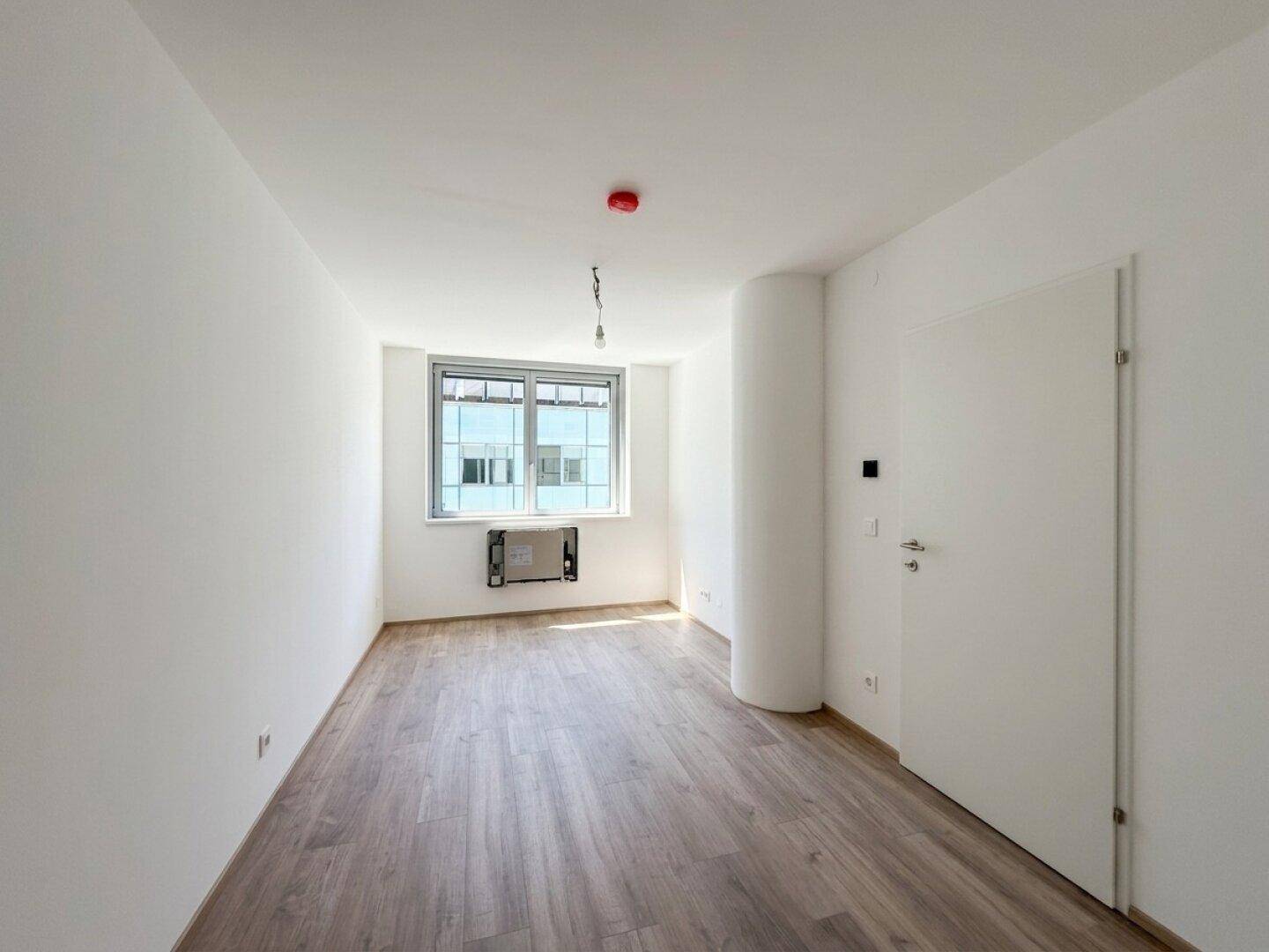 Helles Schlafzimmer mit Laminatboden und einem Fenster, das den Raum gut belichtet.