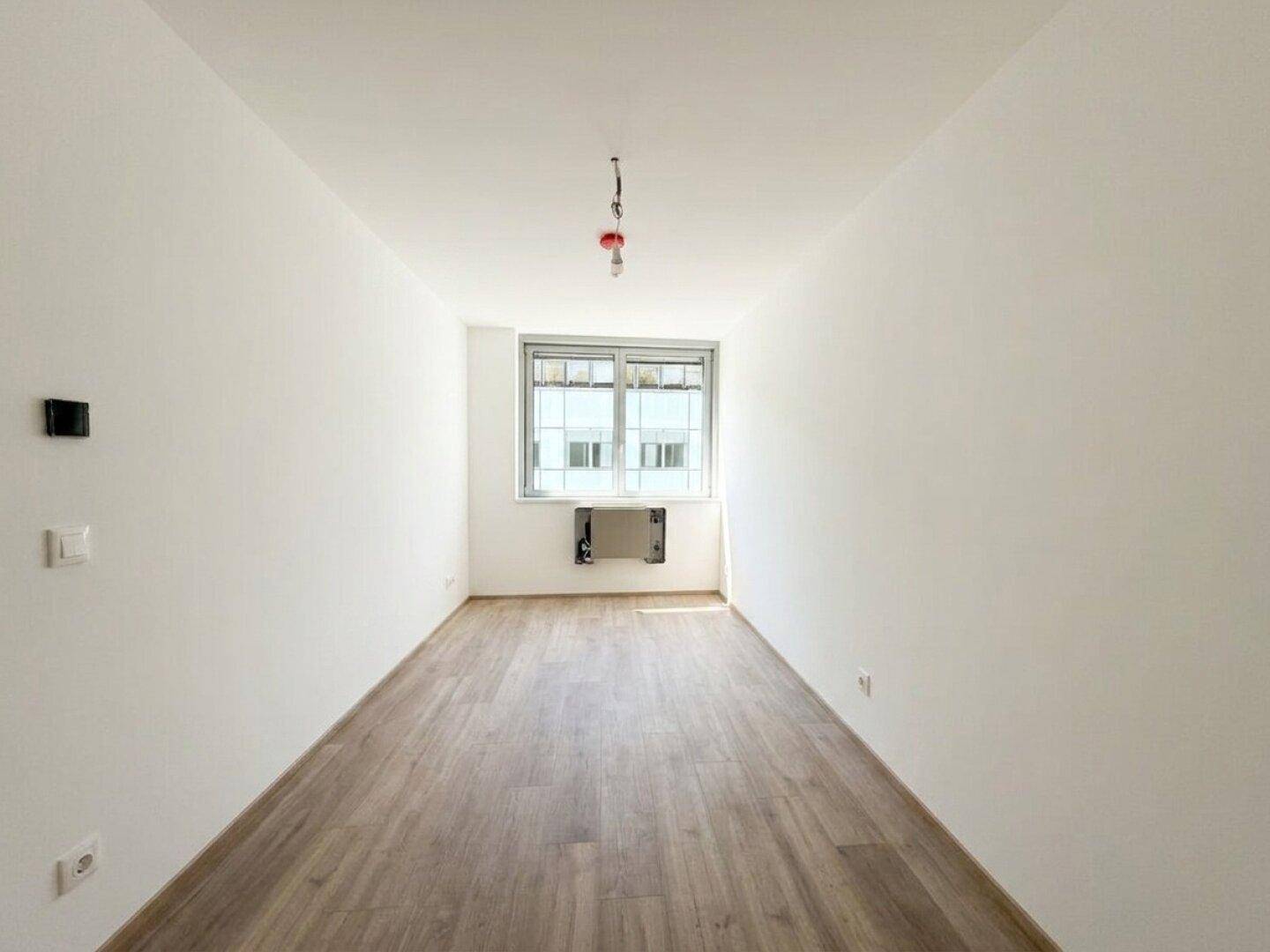 Schmaler Raum mit Laminatboden und einem Fenster, ideal als Schlafzimmer oder Arbeitszimmer.