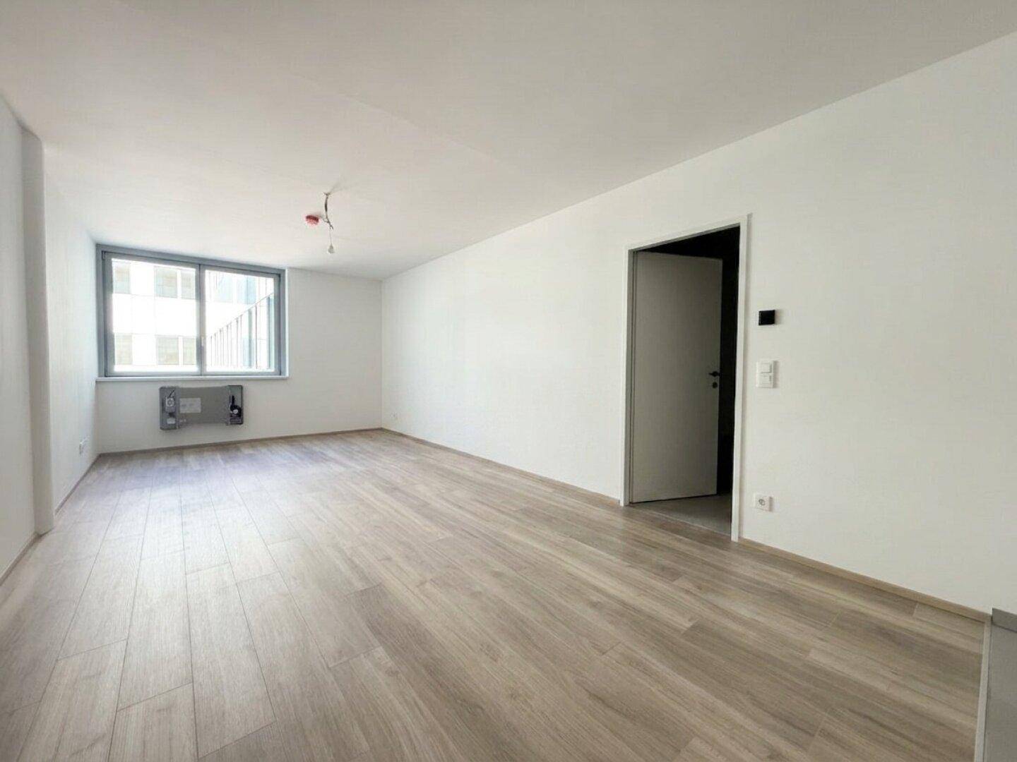 Geräumiges, helles Zimmer mit großen Fenstern und neuem Bodenbelag, ideal für Wohnzwecke.