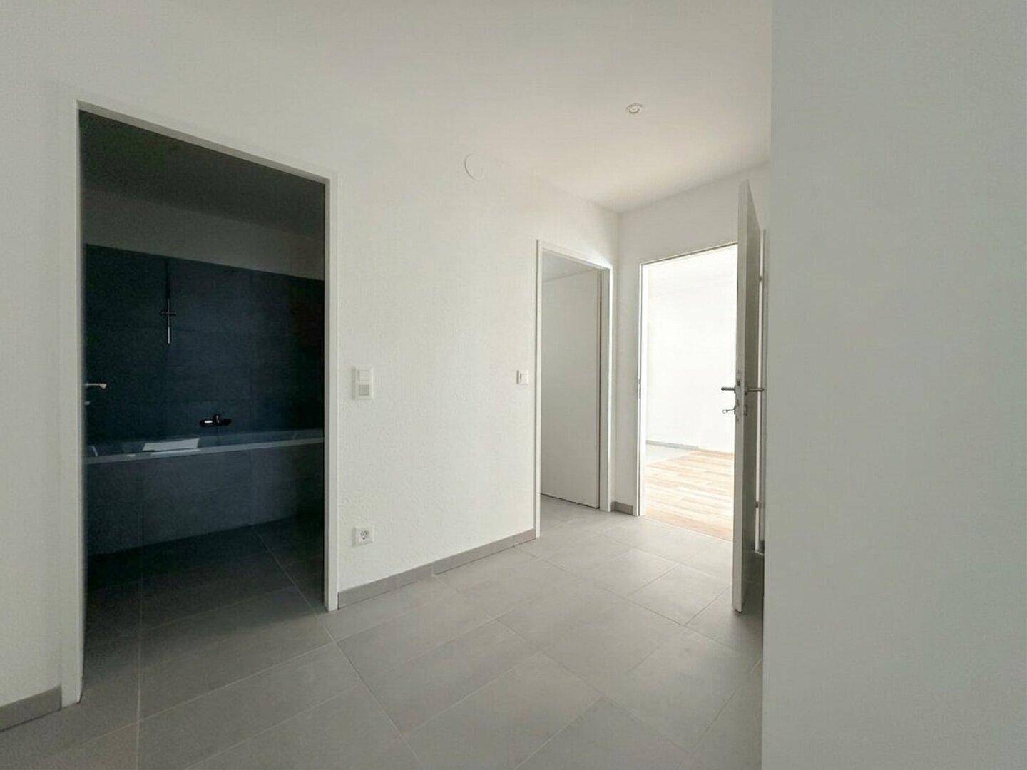 Heller Flur mit grauen Fliesen, der zu verschiedenen Zimmern der Wohnung führt.
