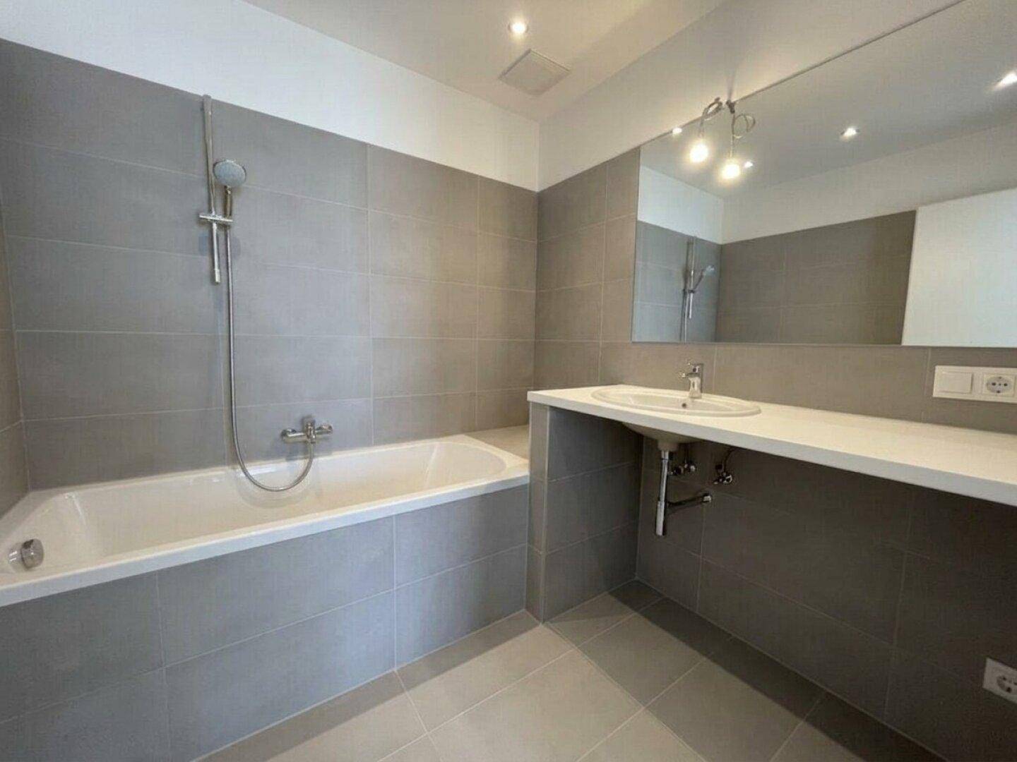 Modernes Badezimmer mit grauen Fliesen, Badewanne und einem einzelnen Waschbecken.