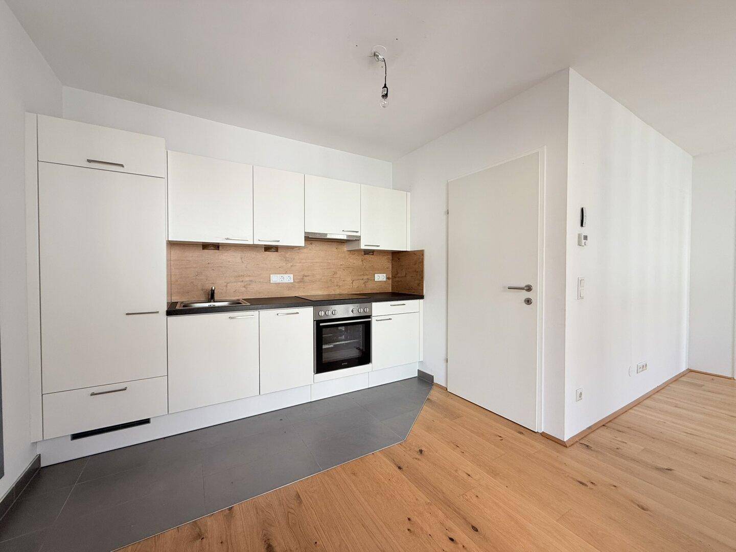 Moderne Einbauküche mit weißen Schränken, dunkler Arbeitsplatte und Holzakzenten.