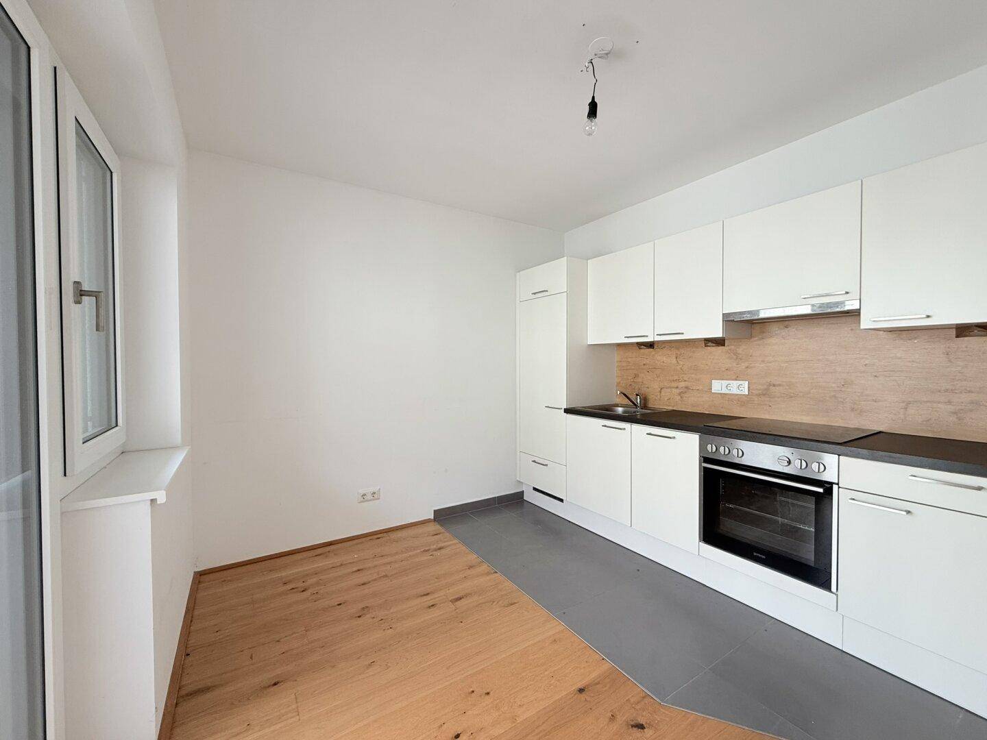 Helle Einbauküche mit weißen Fronten, integriertem Backofen und Blick nach draußen.
