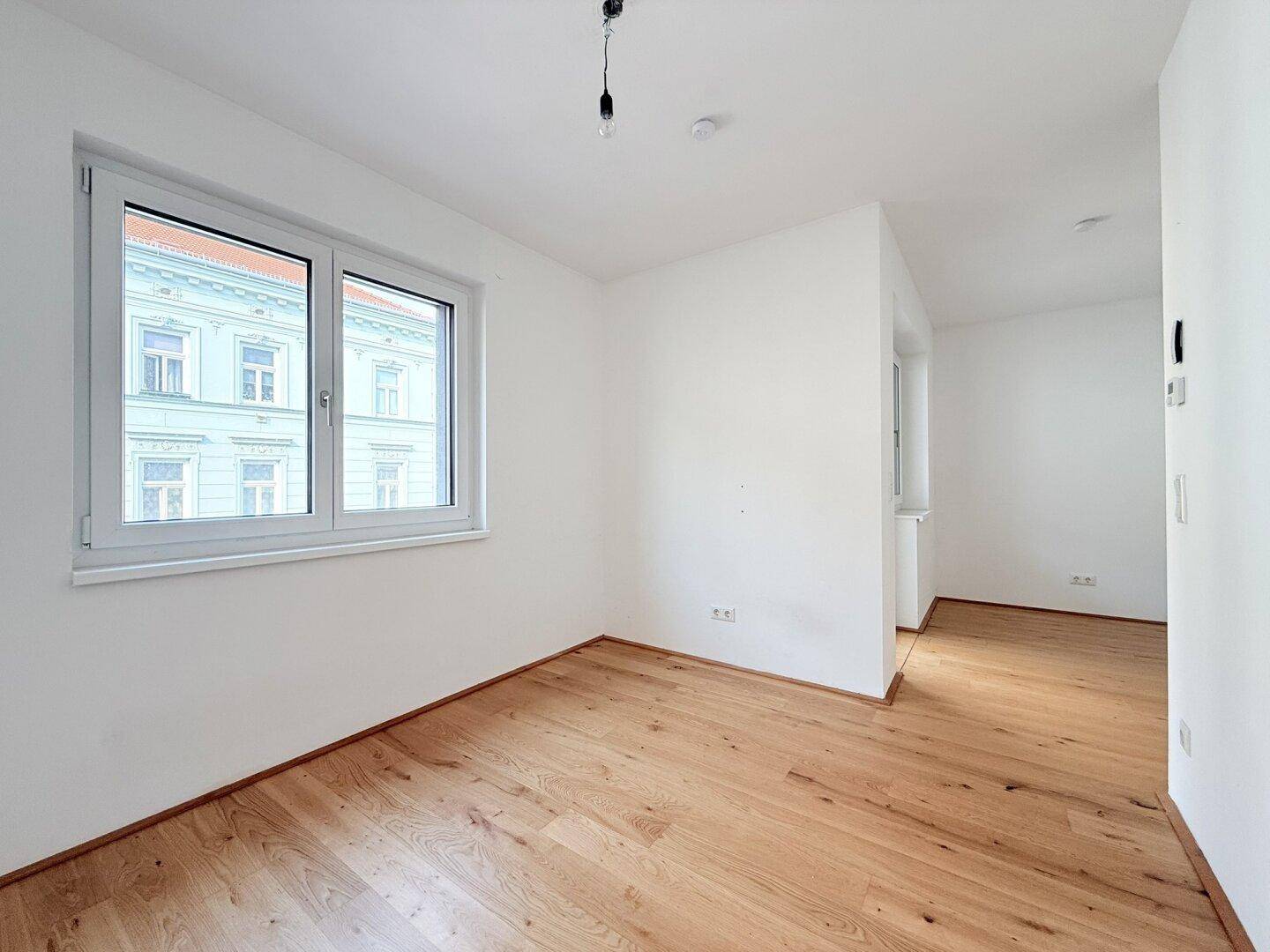 Geräumiges Zimmer mit Holzboden und großem Fenster, das viel Tageslicht hereinlässt.