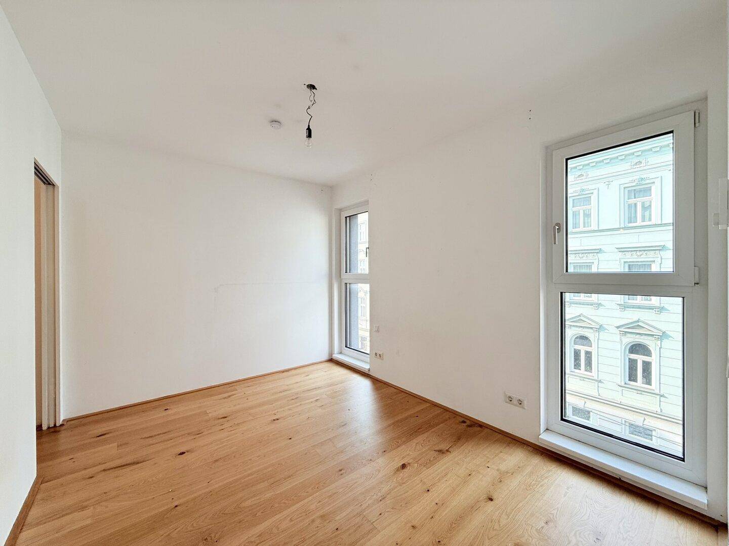 Helles Zimmer mit zwei Fenstern und Holzboden, bietet einen urbanen Ausblick.