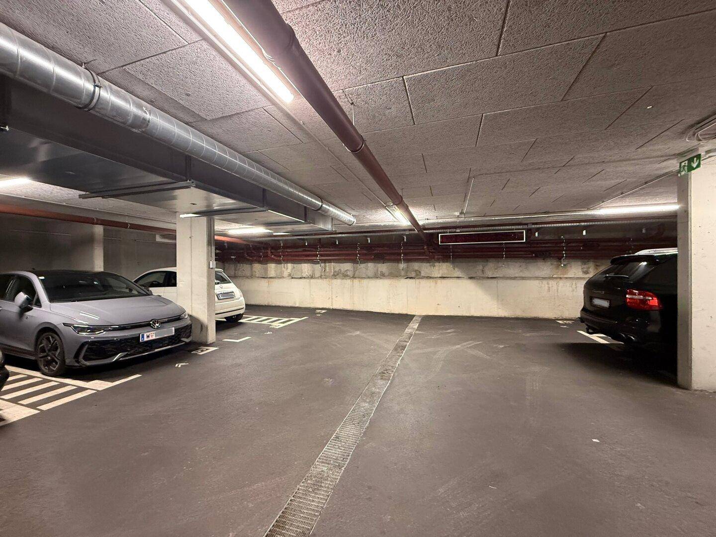 Geräumige Tiefgarage mit ausreichend Parkplätzen, funktionaler Beleuchtung und sichtbaren Leitungen.