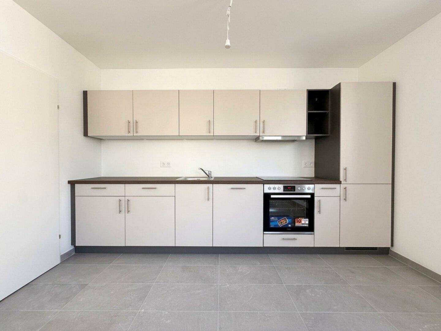 Moderne Einbauküche mit hellgrauen Schränken, integriertem Backofen und Dunstabzugshaube, auf Fliesenboden.