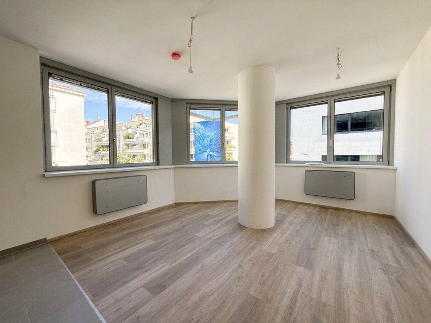 Geräumiger Wohnbereich mit vielen Fenstern und einem zentralen Pfeiler, ausgestattet mit Laminatboden.
