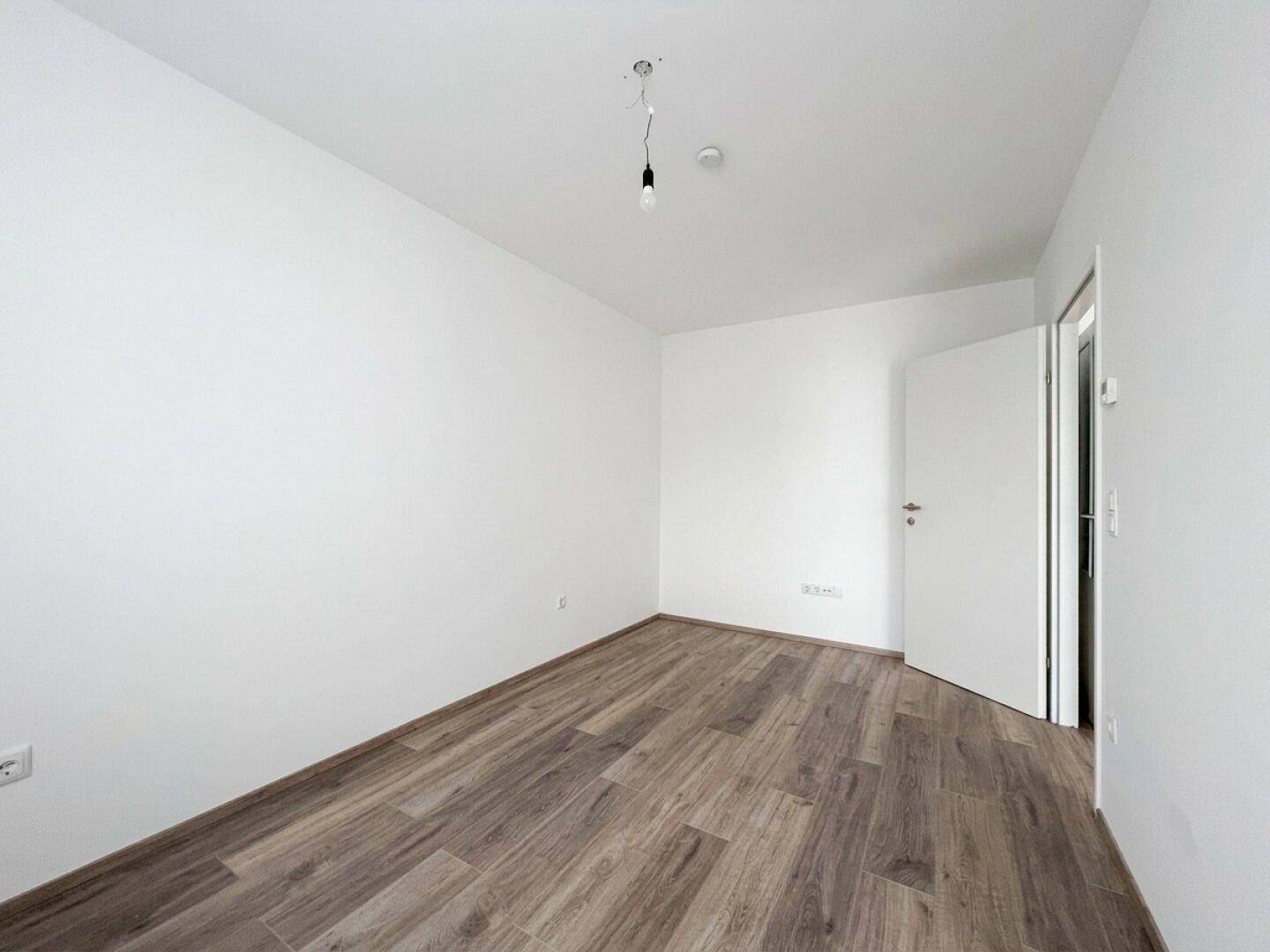Leeres Zimmer mit Holzboden und weiß gestrichenen Wänden, ideal als Schlaf- oder Arbeitszimmer.