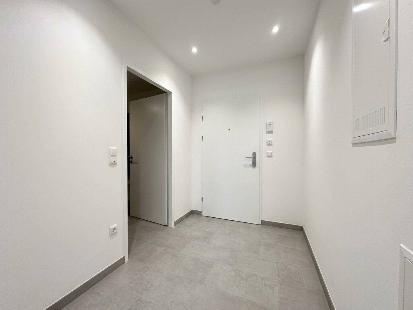 Heller Eingangsbereich mit Fliesenboden und moderner Deckenbeleuchtung in einem Neubau.