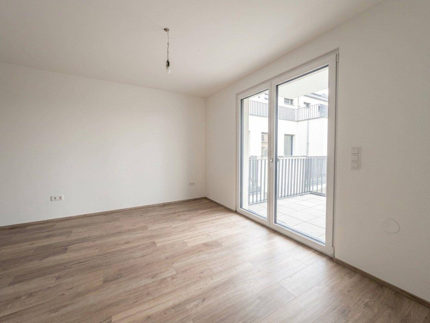 Geräumiges Zimmer mit großen Fenstern und Blick auf den Balkon, ideal für Wohnzwecke.