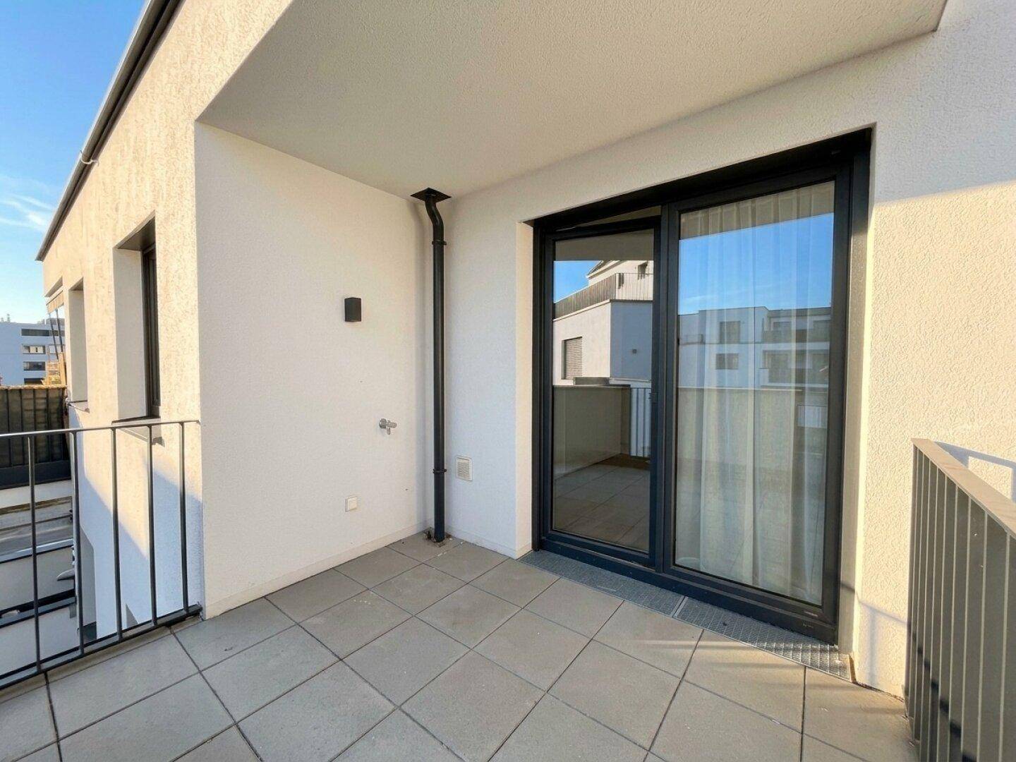 Sonniger Balkon mit Fliesenboden und Blick auf die umliegenden modernen Gebäude.