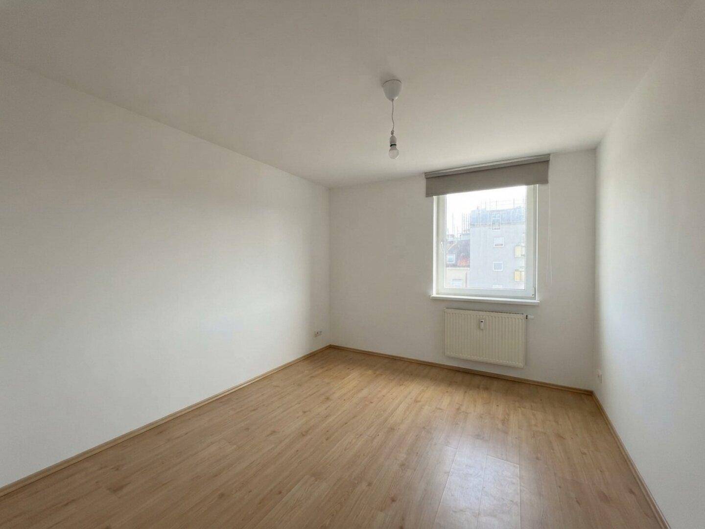 Helles Schlafzimmer mit Parkettboden und einem Fenster mit Blick nach draußen.