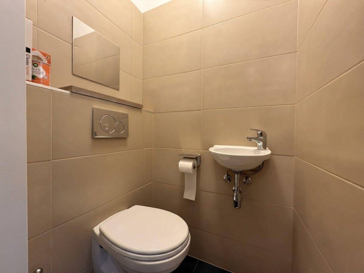 Kleines Gäste-WC mit Wand-WC, kleinem Waschbecken und beigefarbenen Fliesen.