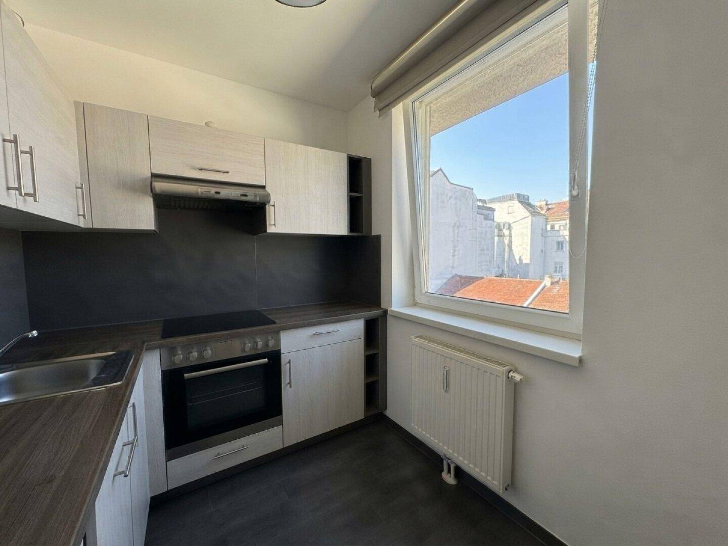 Funktionale Küche mit Einbauschränken, Kochfeld und Fenster mit Stadtblick.