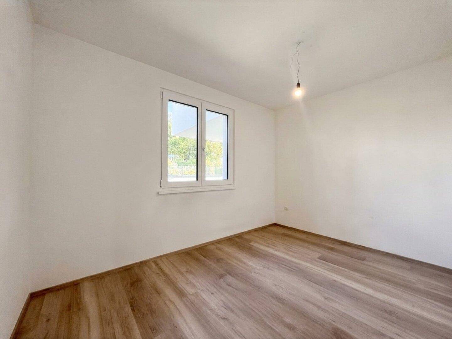 Helles Schlafzimmer mit Laminatboden und großem Fenster, bereit zum Einrichten.