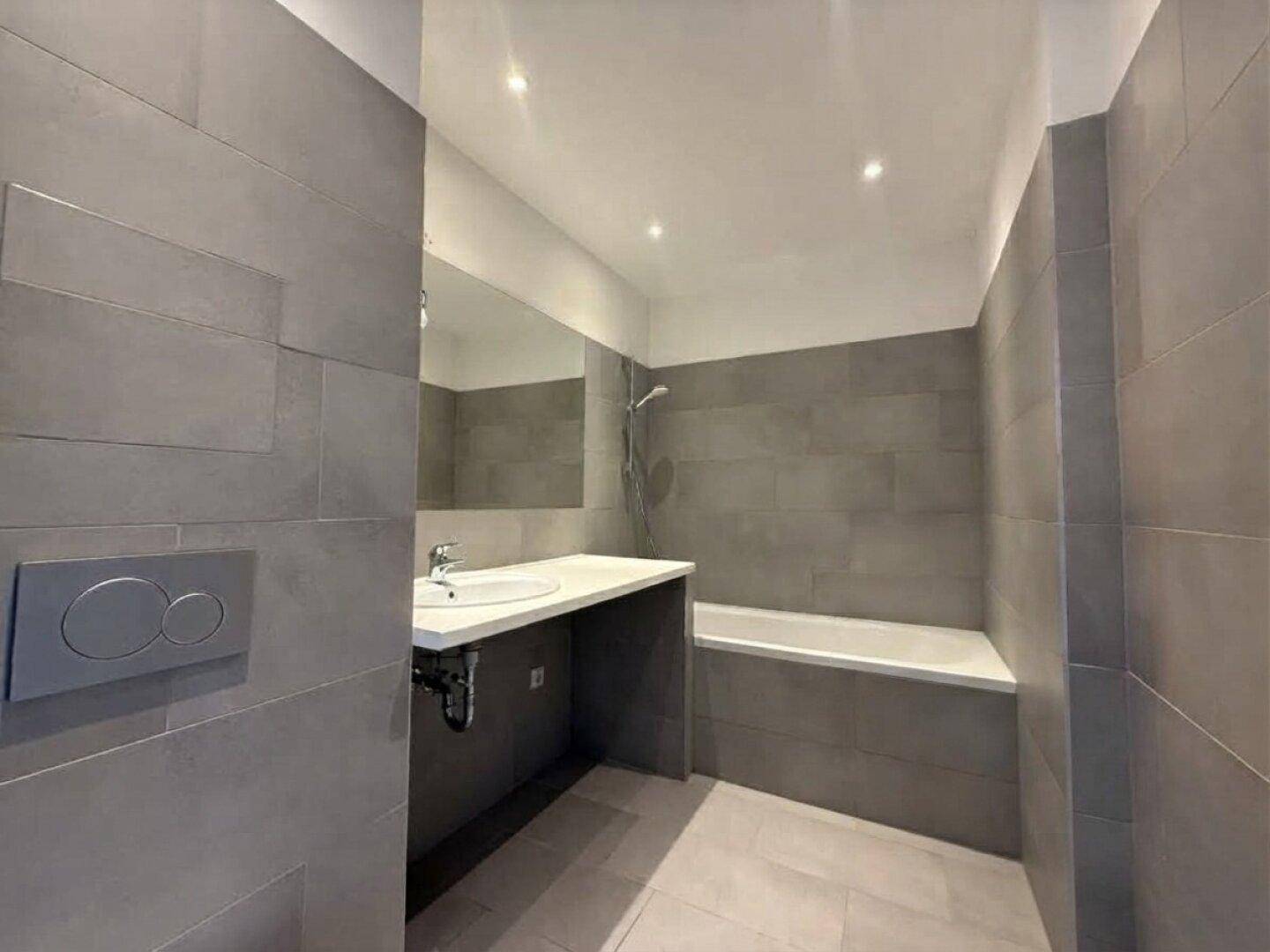 Modernes Badezimmer mit grauen Fliesen, Badewanne und wandmontiertem WC.