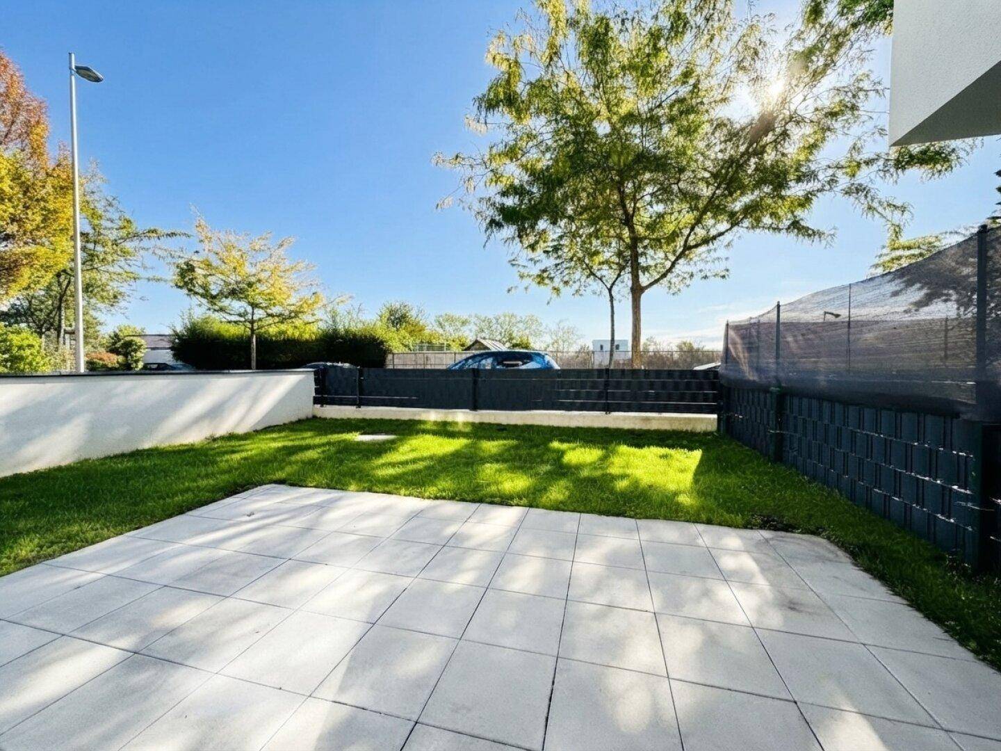 Gepflegter Gartenbereich mit Rasenfläche und gepflasterter Terrasse unter blauem Himmel.